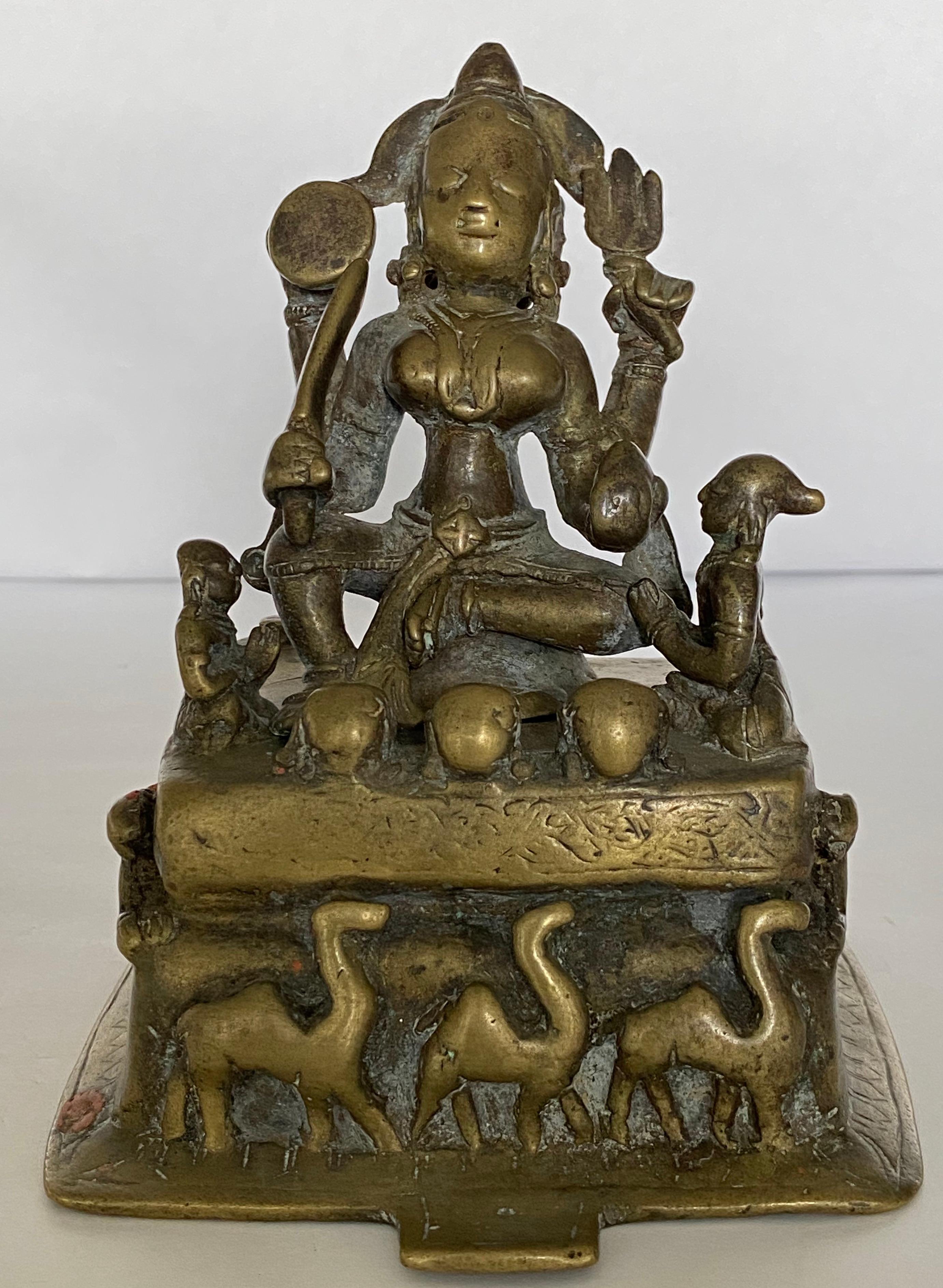 Durga è una dea guerriera nella cultura indù, è la protettrice dei buoni raffigurata qui a più armi con una spada, un tridente, una ruota e un gioiello tra le mani. È affiancata da due assistenti con una fila di teschi ai suoi piedi. La base