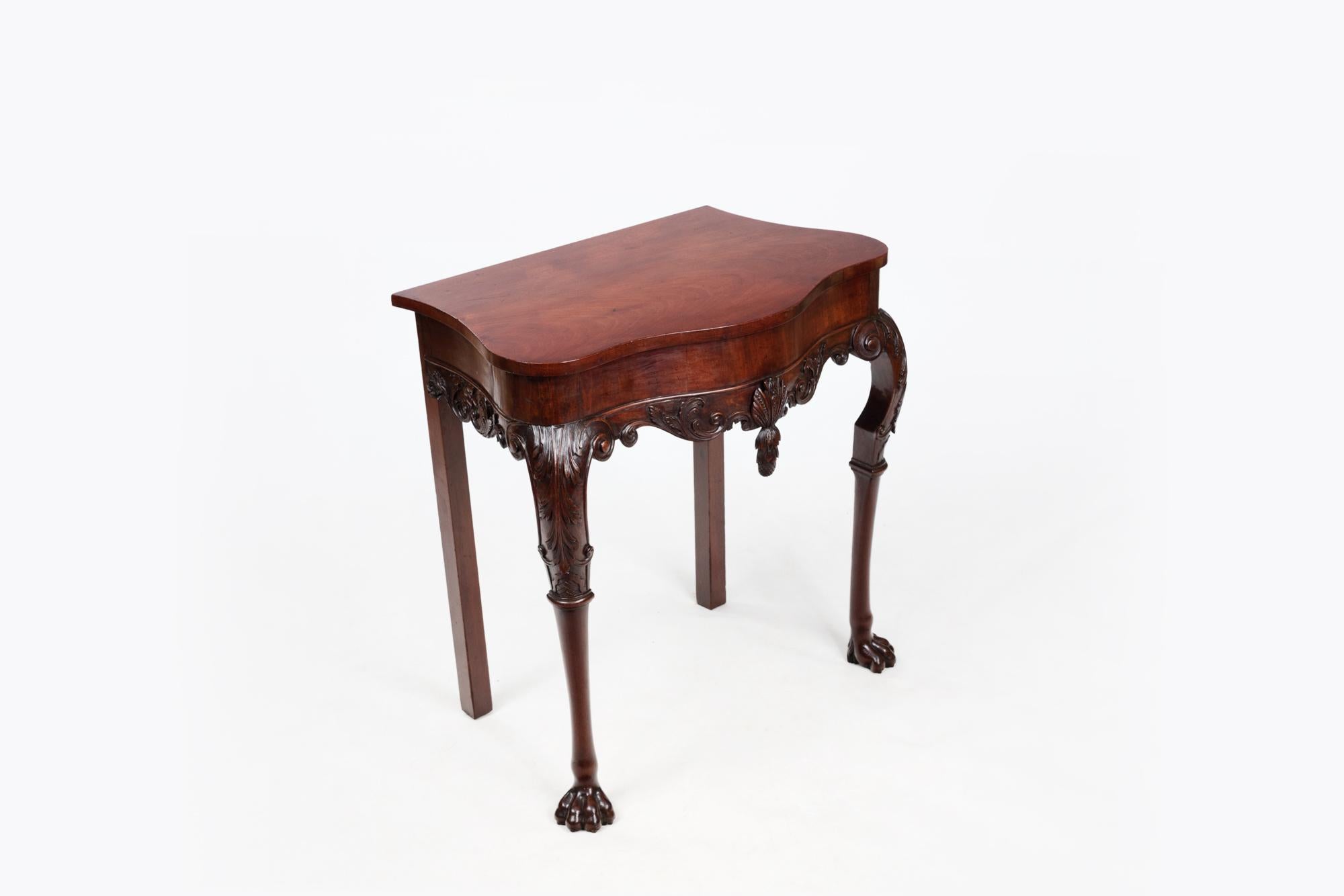 Mid-18th Century Irish walnut and mahogany serpentine shaped console table. The top above a deep frieze, centred by a shell pineapple pendant and flanked by scrolls. Centred by flower heads on leaf capped scroll hipped legs, terminating in lion paw