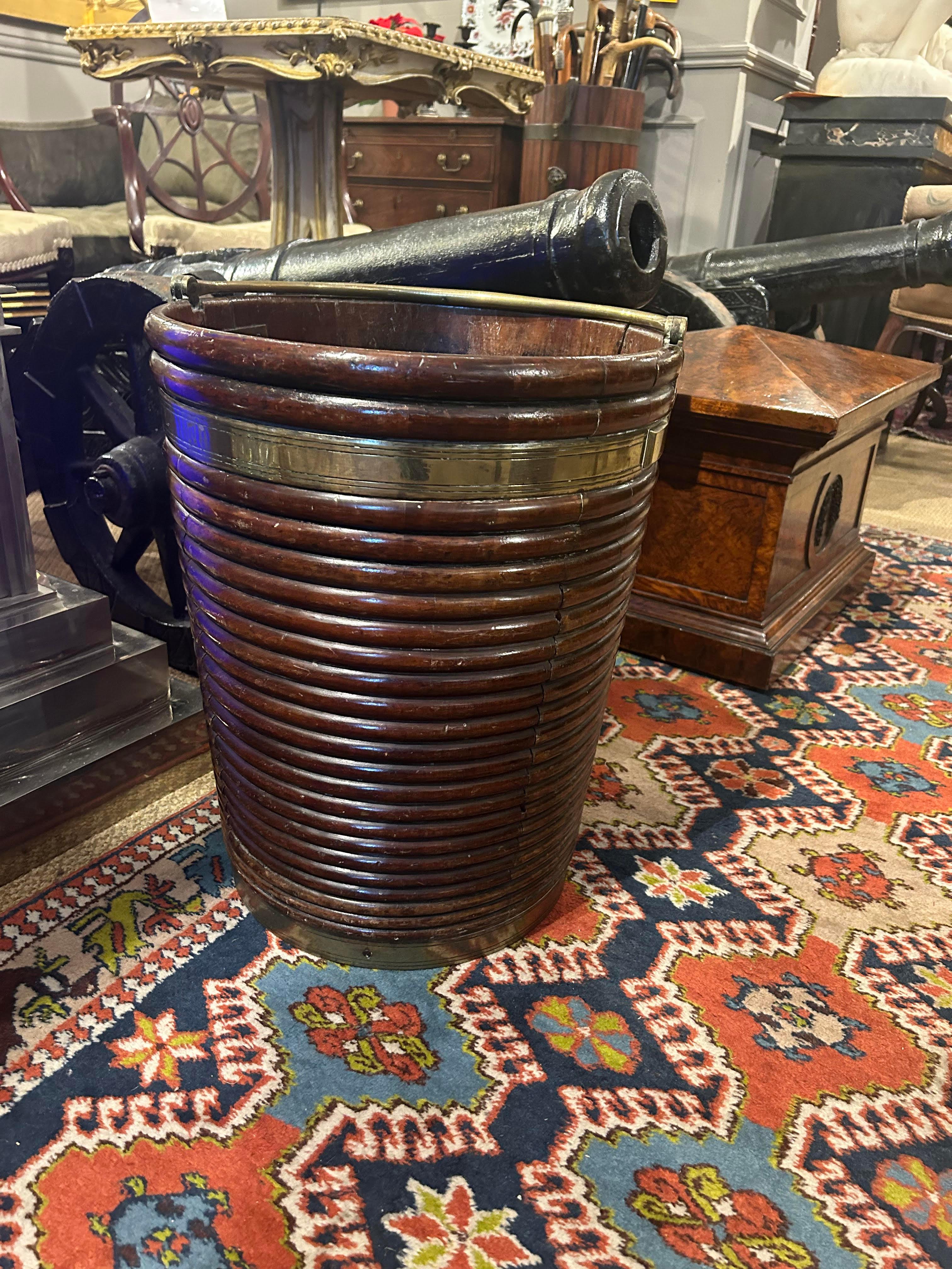 18th Century Irish George III mahogany and brass bound turf bucket with graduated ring-turned carving of good size and unusual design with unique brass swing handle and body of tapered construction.
