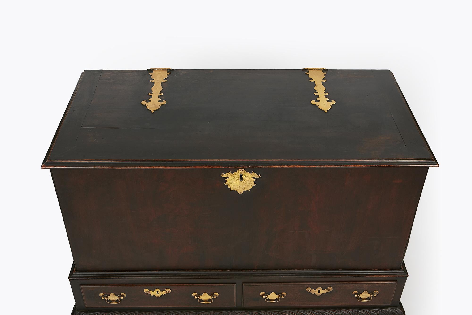 18th century Irish mahogany blanket chest supported over heavily carved acanthus stand with two short drawers terminating on hairy paw feet decorated with ornate brass fittings throughout.