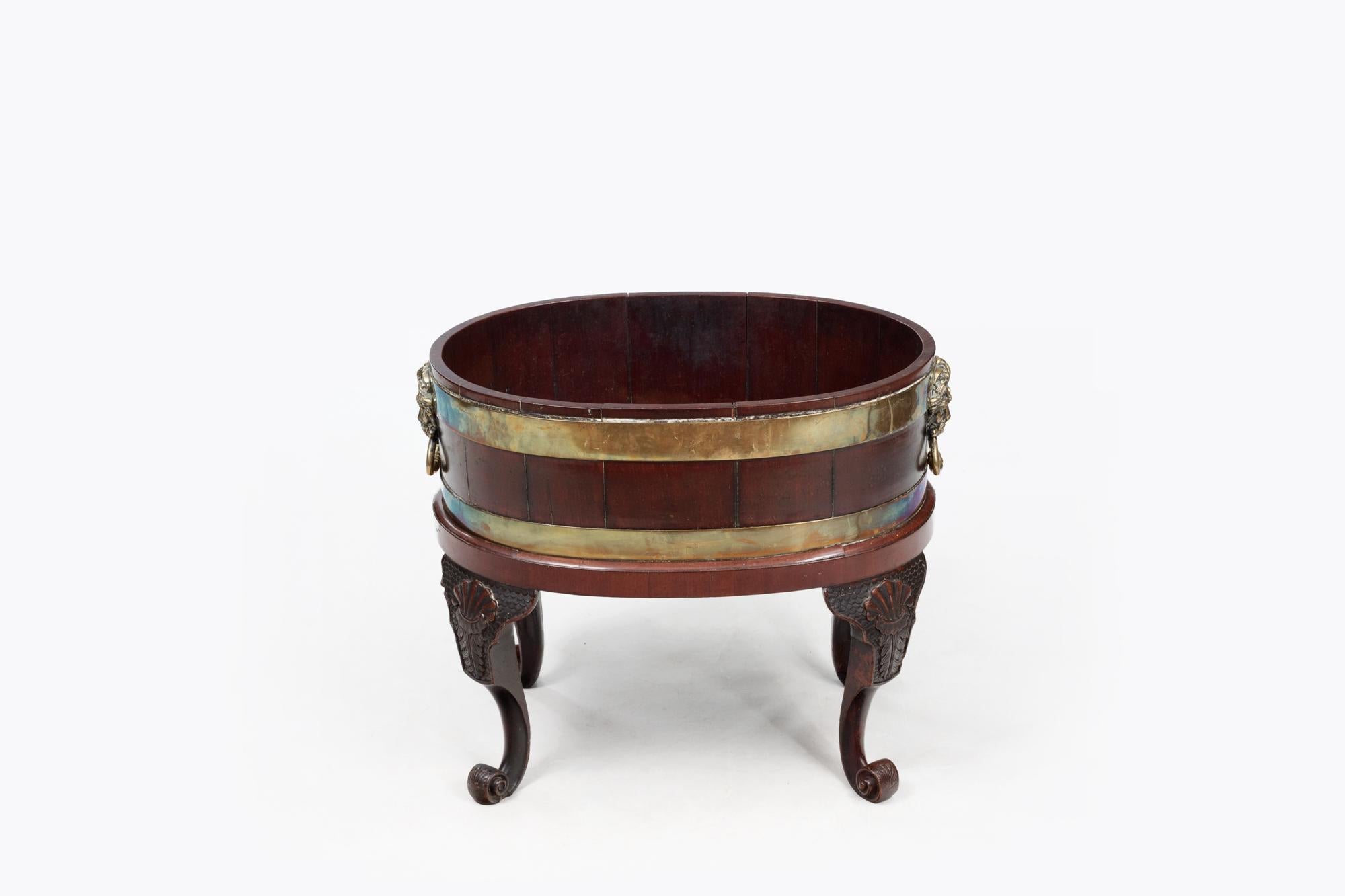 18th Century Irish mahogany oval brass-bound jardiniere with lion mask handles. The planter sits on four cabriole legs featuring carved shell design to the knees and terminating on scroll feet.