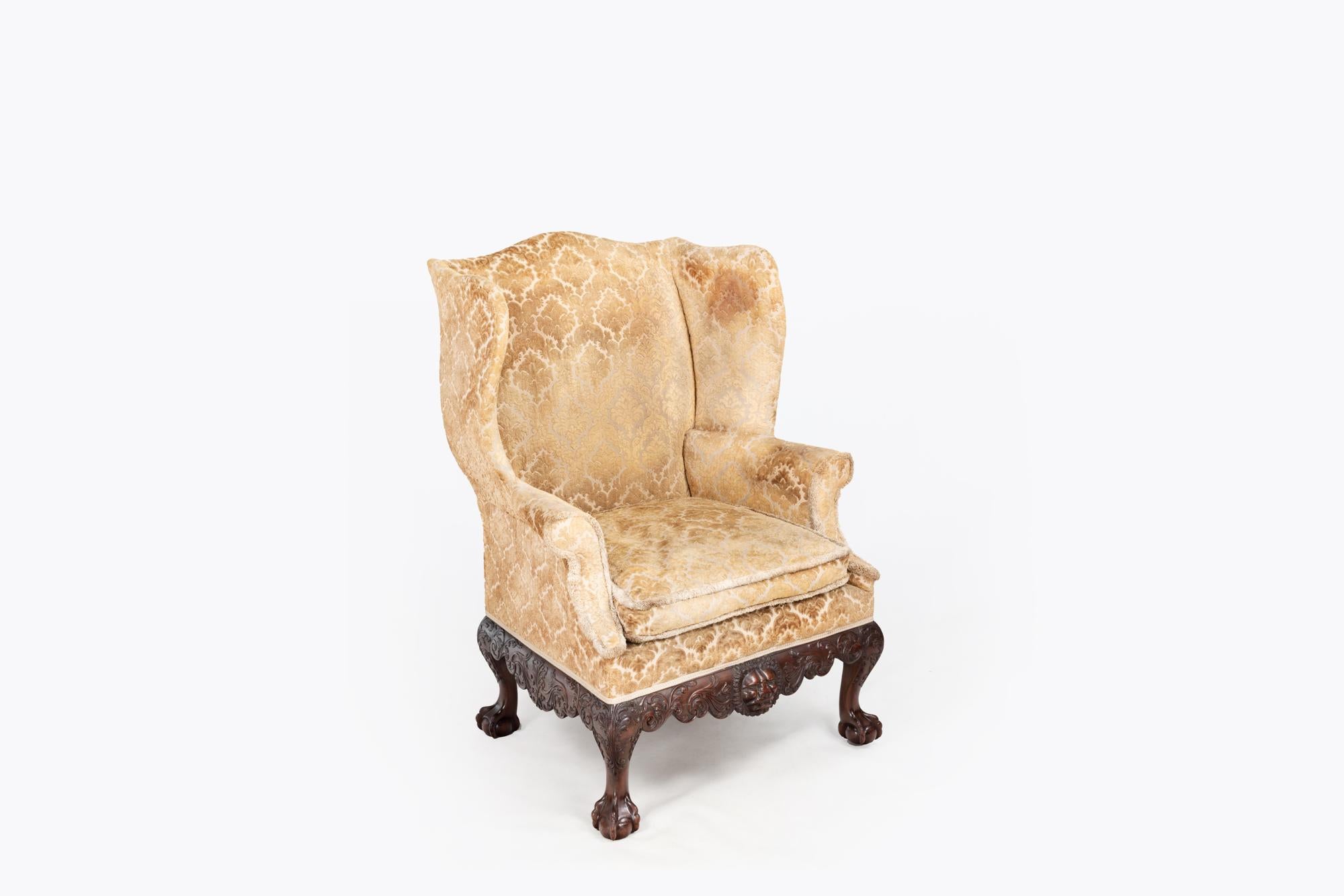 18th Century Irish wing chair ornately carved mahogany apron with scrolling foliate and central lion head motif. Supported on cabriole legs terminating in ball & claw feet.