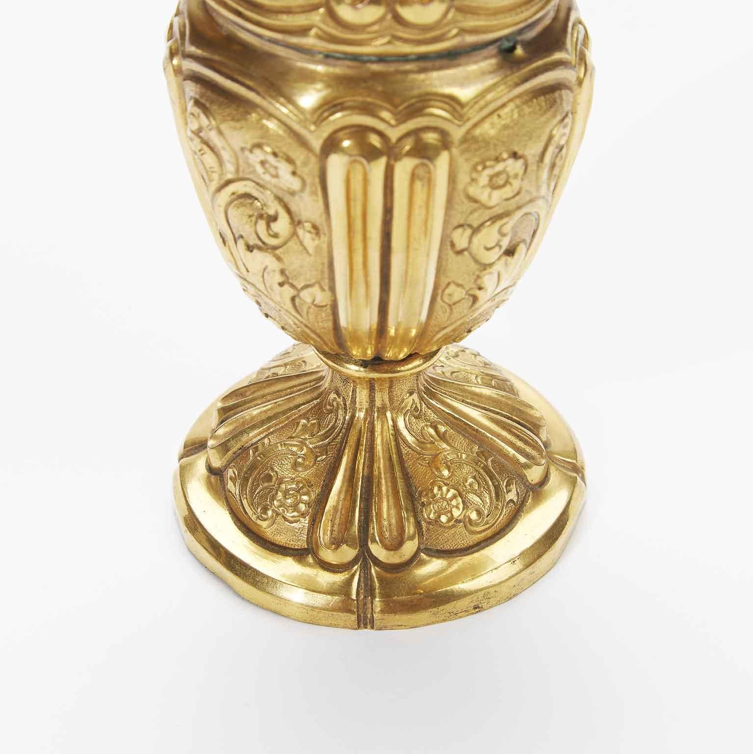 Superbe aiguière italienne en cuivre doré datant du XVIIIe siècle, dont le corps circulaire présente un décor quadripartite défini par le repoussé d'un double cadre vertical nervuré qui encadre des tableaux décorés de rinceaux floraux ; le fond de