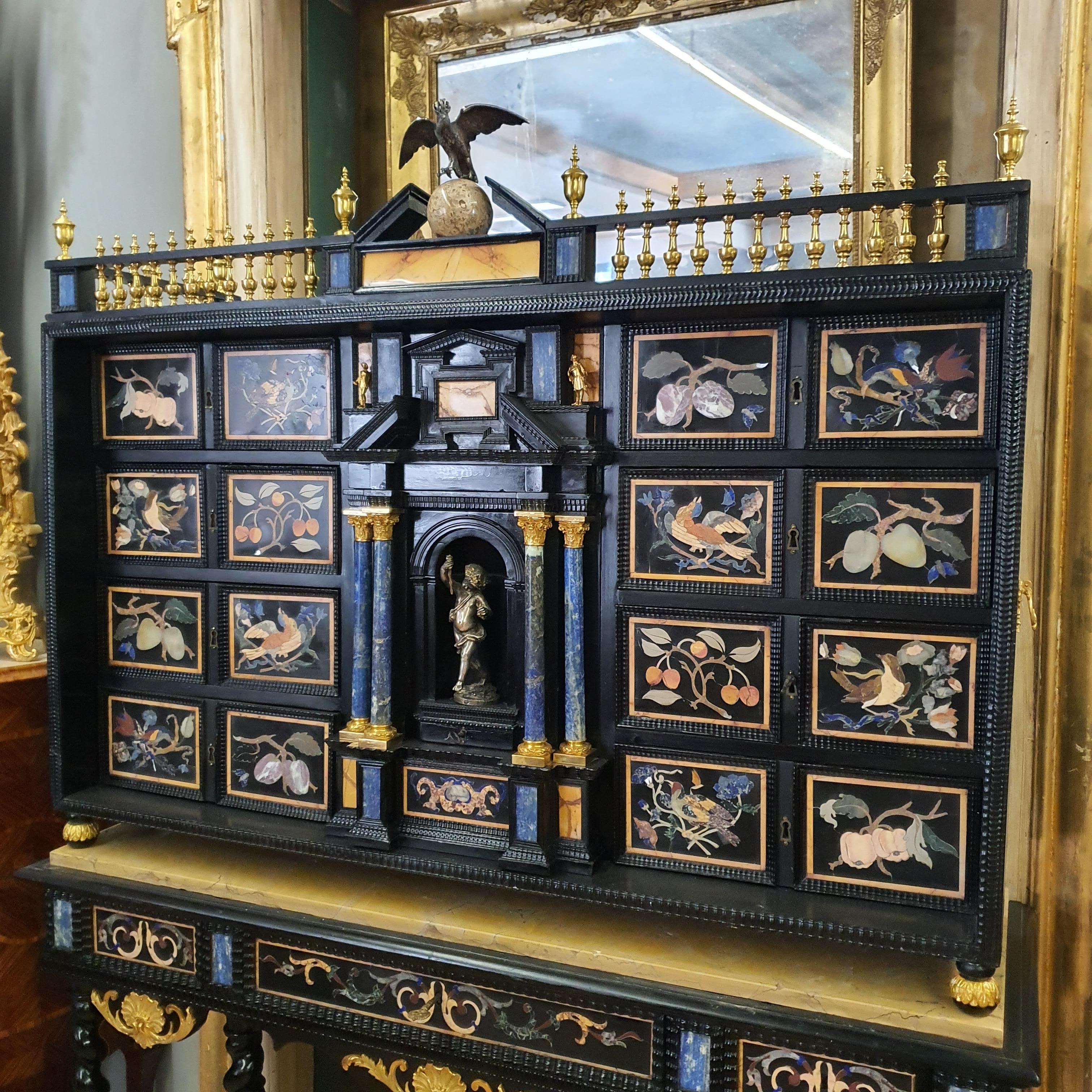 Prestigious Italian cabinet on stand with semi-precious stones, gilded bronze and silver.
Furniture made of wood veneered in ebony, tiles inlaid with semi-precious stones adorn the front of the furniture in which we also find four columns in lapis