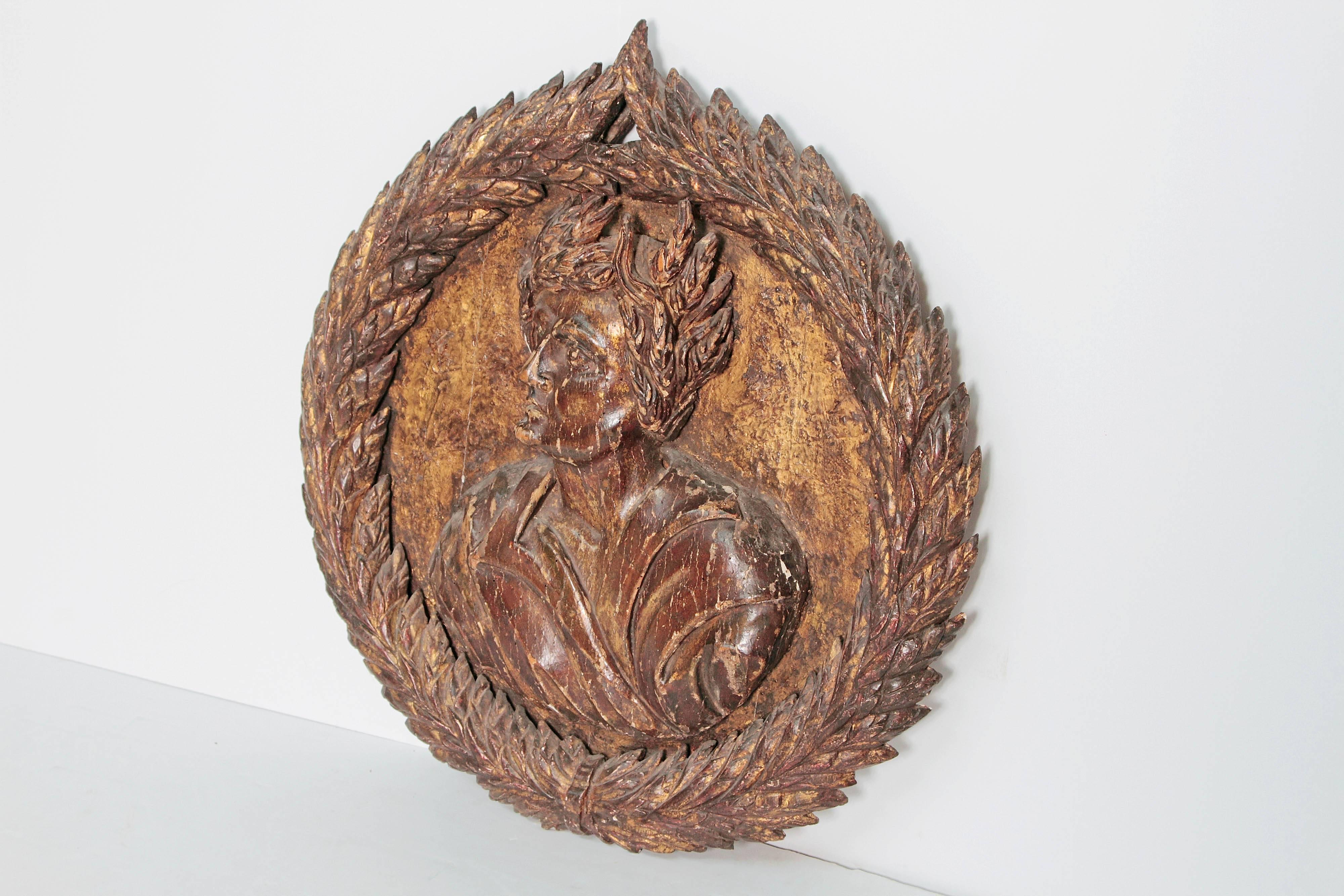 A carved giltwood roundel with laurel leaf wreath. Man's face in center, 18th century, Italy.