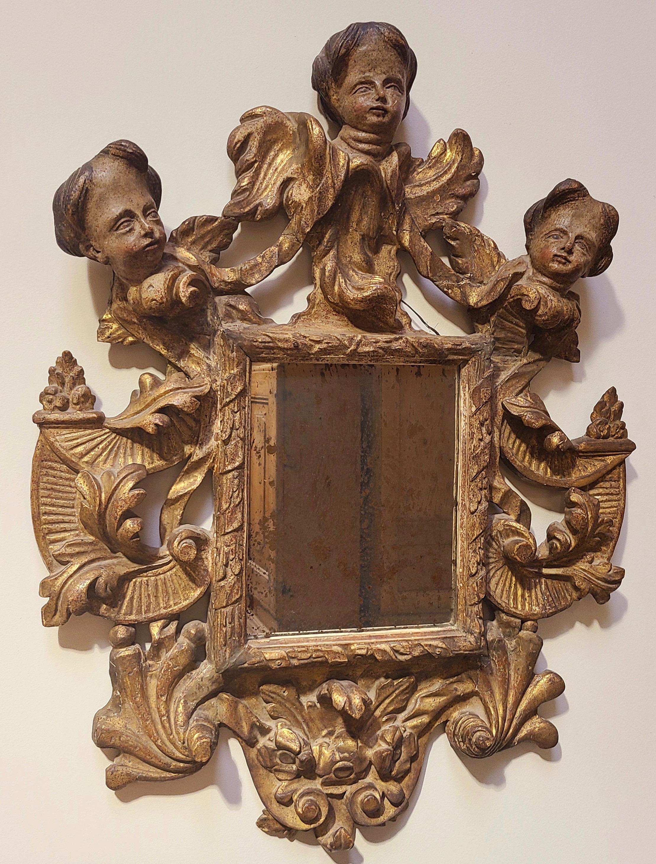 Beautifully carved and gold leafed wood mirror with three cherubs holding garland swags, and the frame having centuries old patina. In remarkable condition.
Original hand forged iron loop for hanging.
Italy, 18th century.

Old replacement