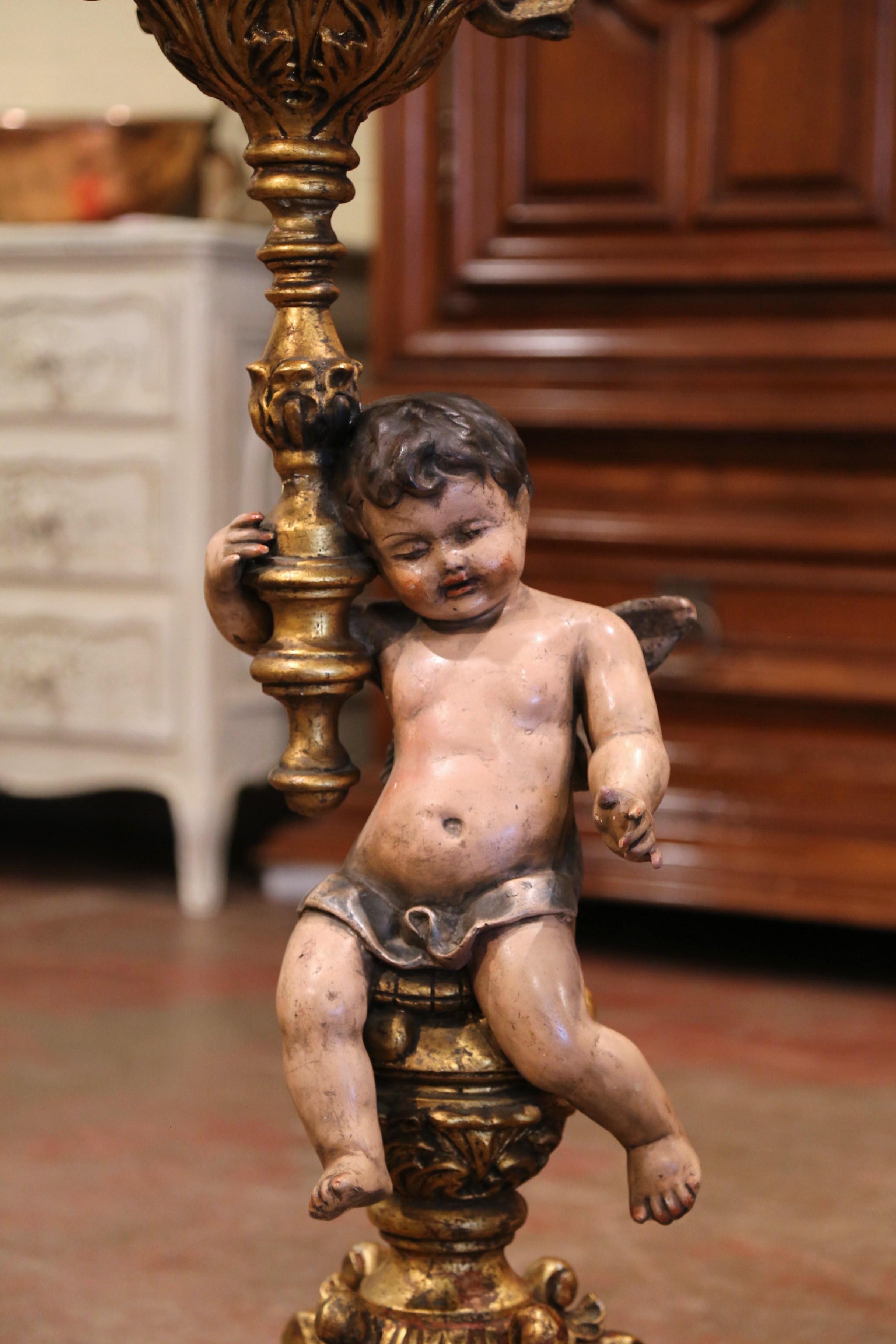 Decorate a den or study with this elegant, antique floor lamp; crafted in Italy, circa 1780, the lamp features a hand carved painted cherub figure seated on a round wood base decorated with paw feet at the base; the putti are holding a five-arm