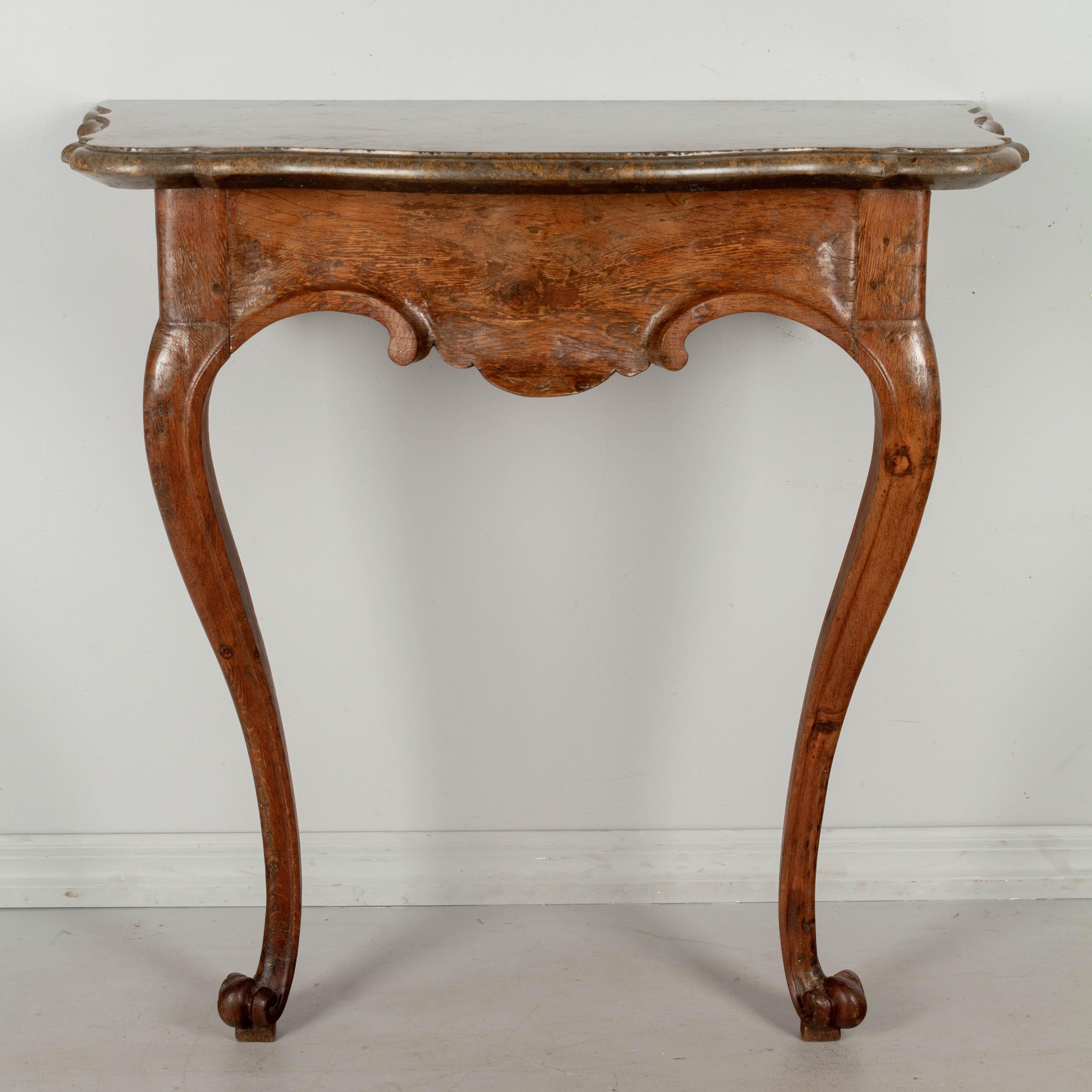 An 18th century Italian carved oak, marble-top console table. Sculptural base made from thick planks with hand-carved scrolls and cabriole legs ending in paw feet. Original marble top has a beautiful grayish taupe color with warm copper vein. This
