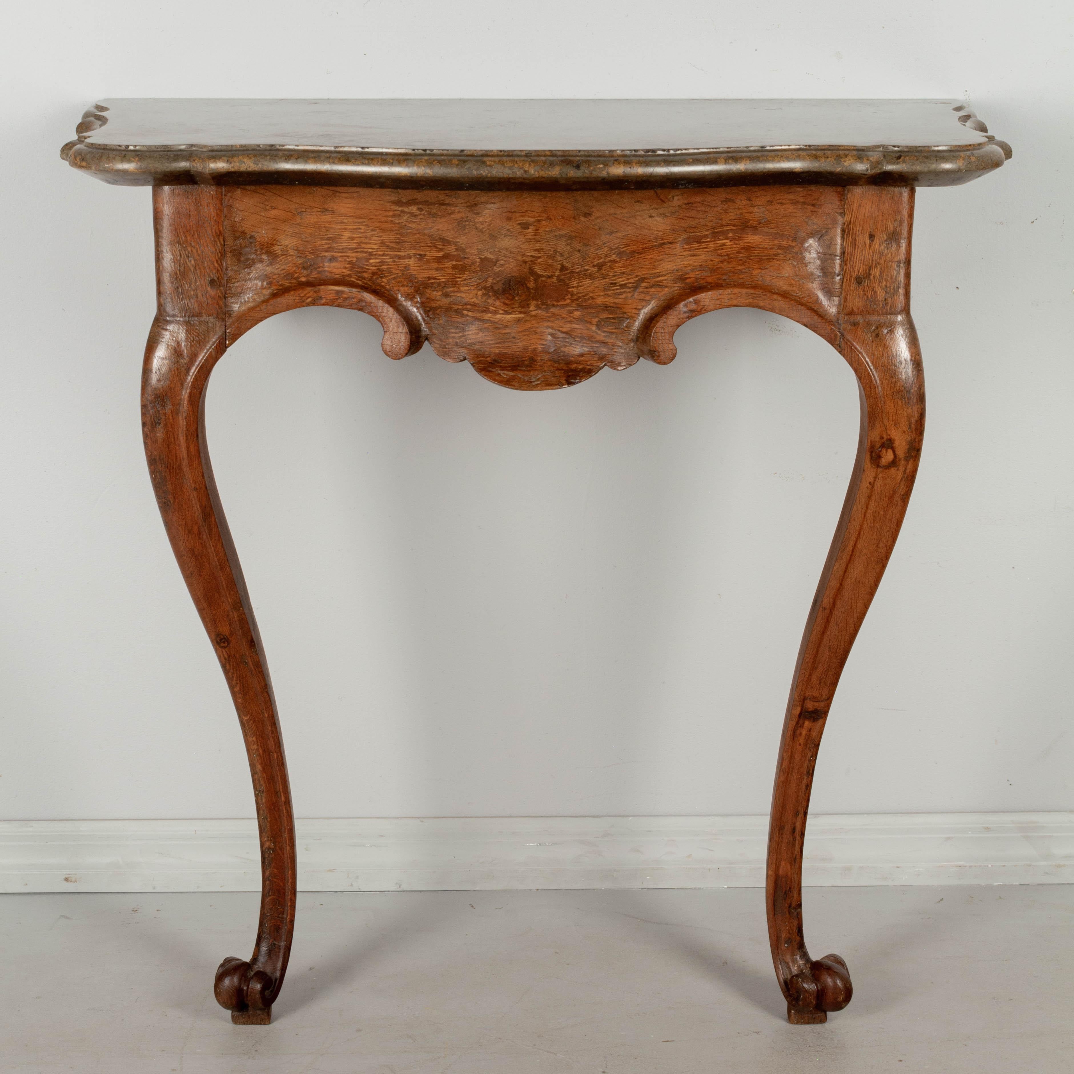 Table console du 18e siècle en chêne sculpté et marbre. Base sculpturale faite de planches épaisses avec des volutes sculptées à la main et des pieds cabriole se terminant par des pieds pattes. Le plateau en marbre d'origine a une belle couleur