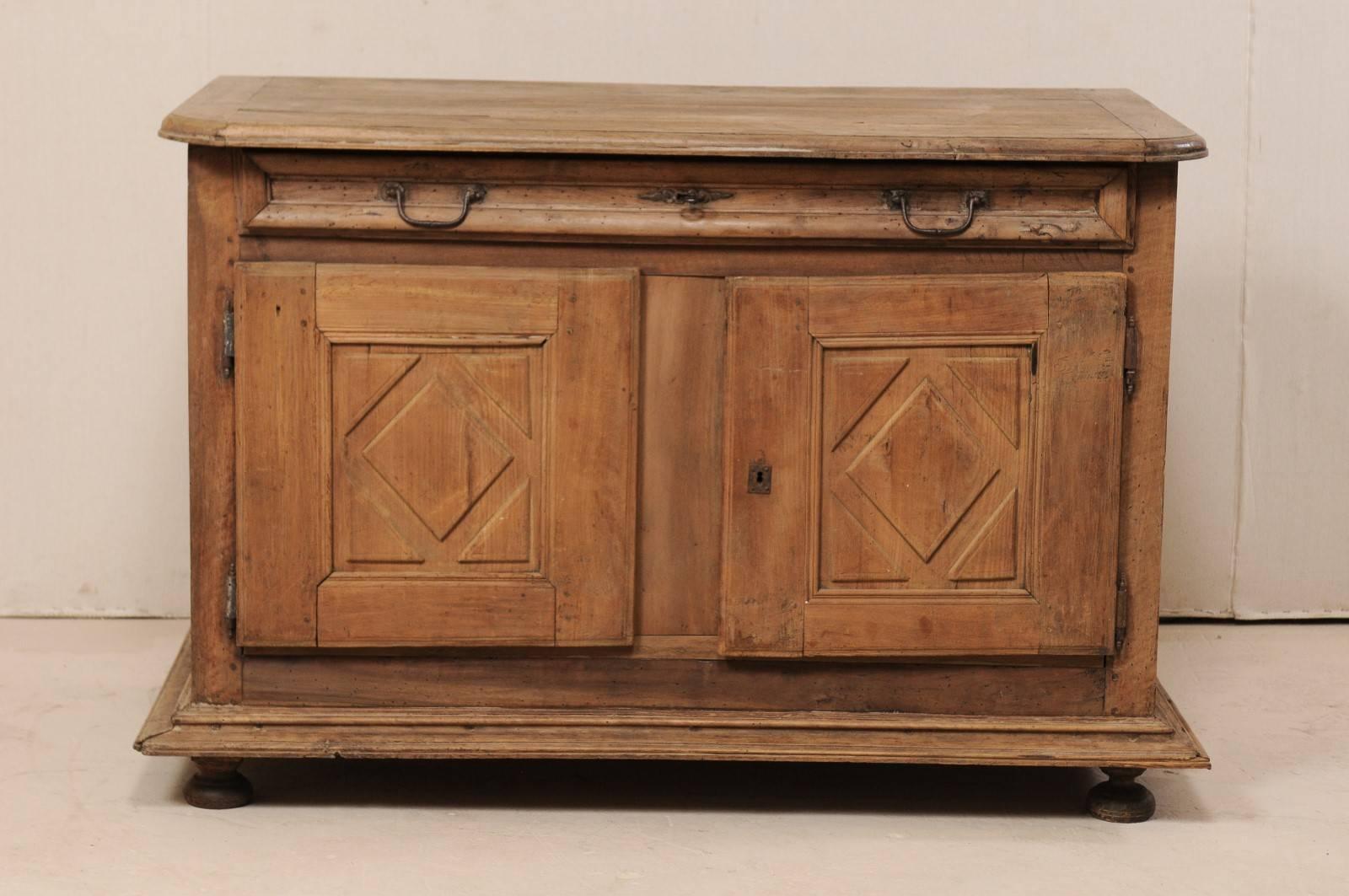 An Italian 18th century two-door credenza of walnut wood. This antique cabinet from Italy features a slightly overhanging top with rounded front corners, atop a slender full length drawer and two doors below which have diamond carved recessed panel