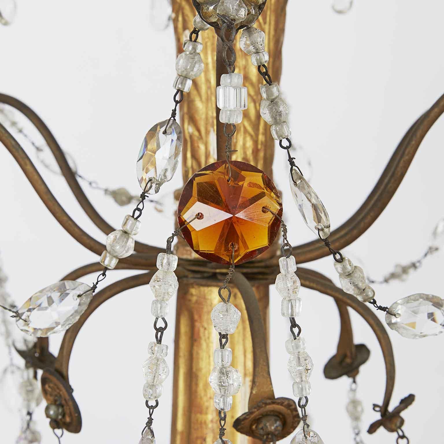 Late 18th century Genoese Empire crystal chandelier with a giltwood carved stem, featuring six curved candle arms draped with cut crystal beads and pendants and decorated with a few amber and clear crystals and original gilded and repoussé brass