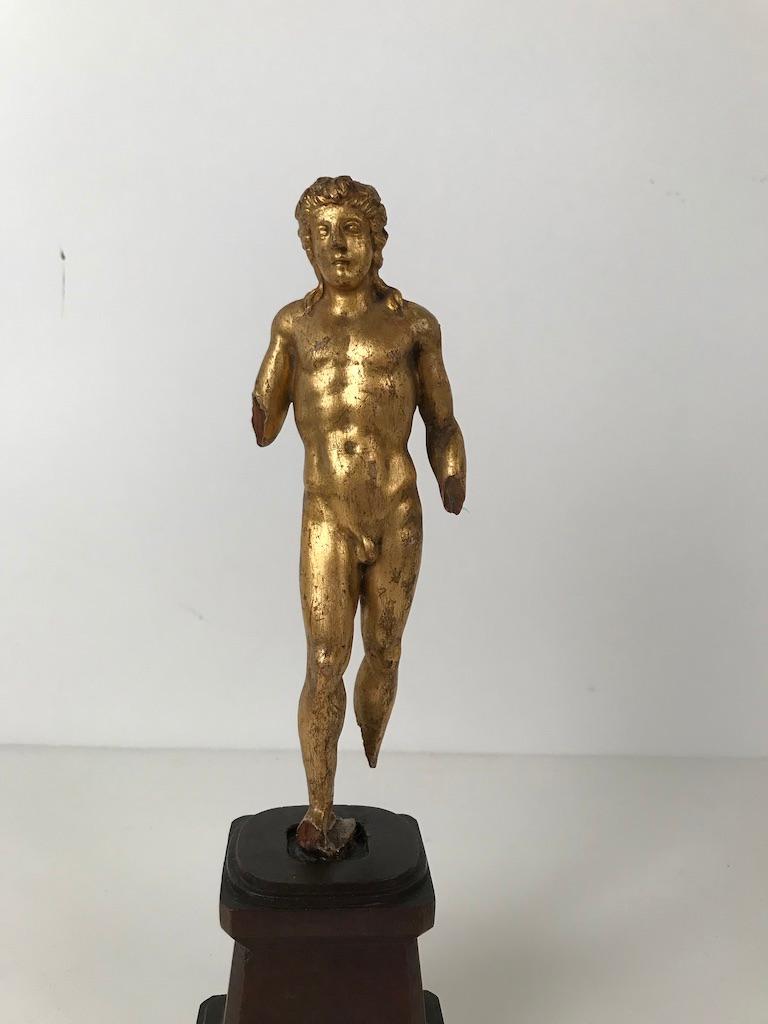 Intriguing small figure of the god Apollo, carved in the round, gilded and mounted on a walnut plinth. Though fragmented, missing both hands and feet, it holds the charm of a Greek or Roman antique marble which it is no doubt modeled after. The