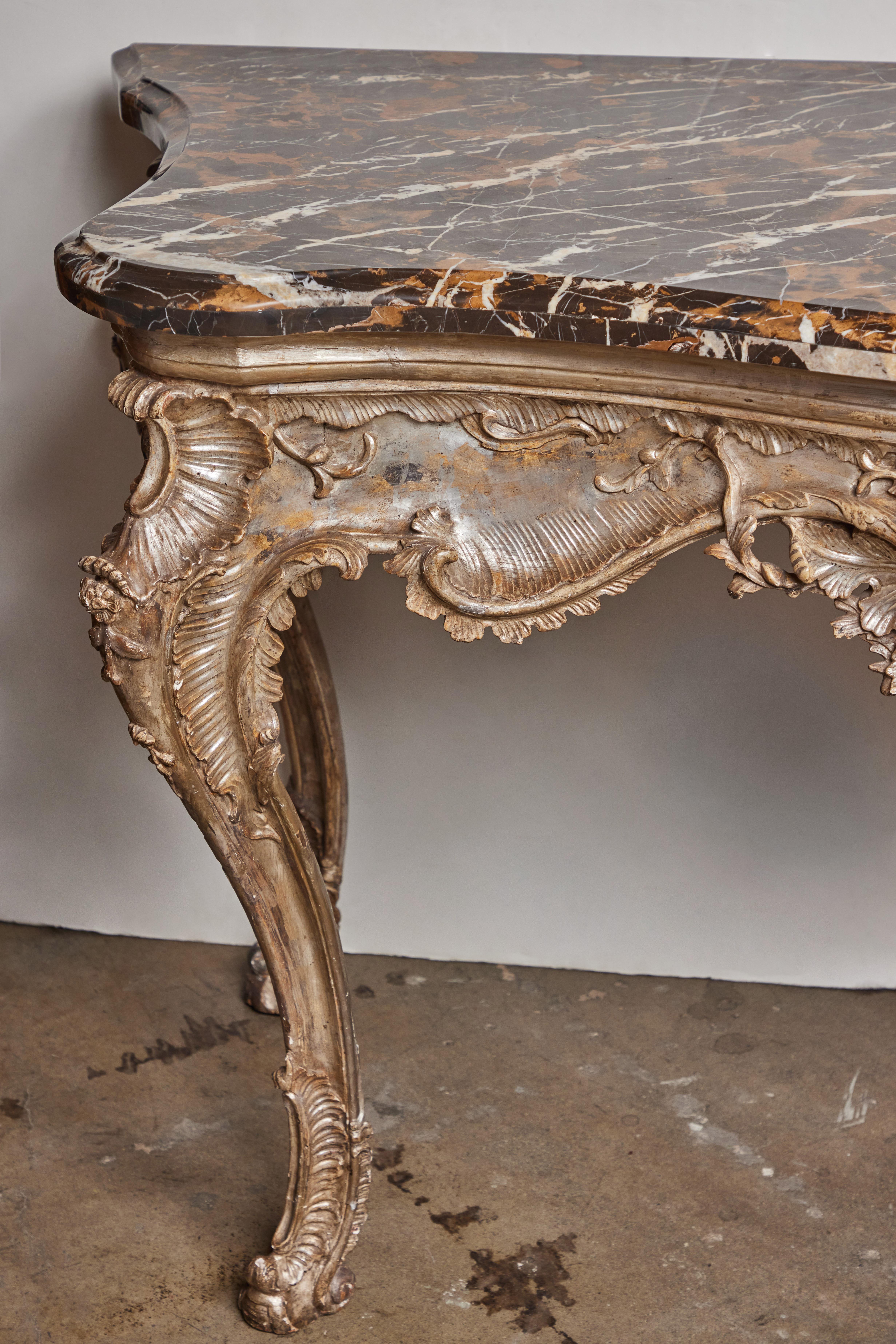 Glorious, hand-carved, gessoed and champagne gilded console with a deep relief, serpentine apron of molded rocaille and foliate forms centered on a shell capped by blossoms. The base features unique, scooped upper legs that then bow forward before