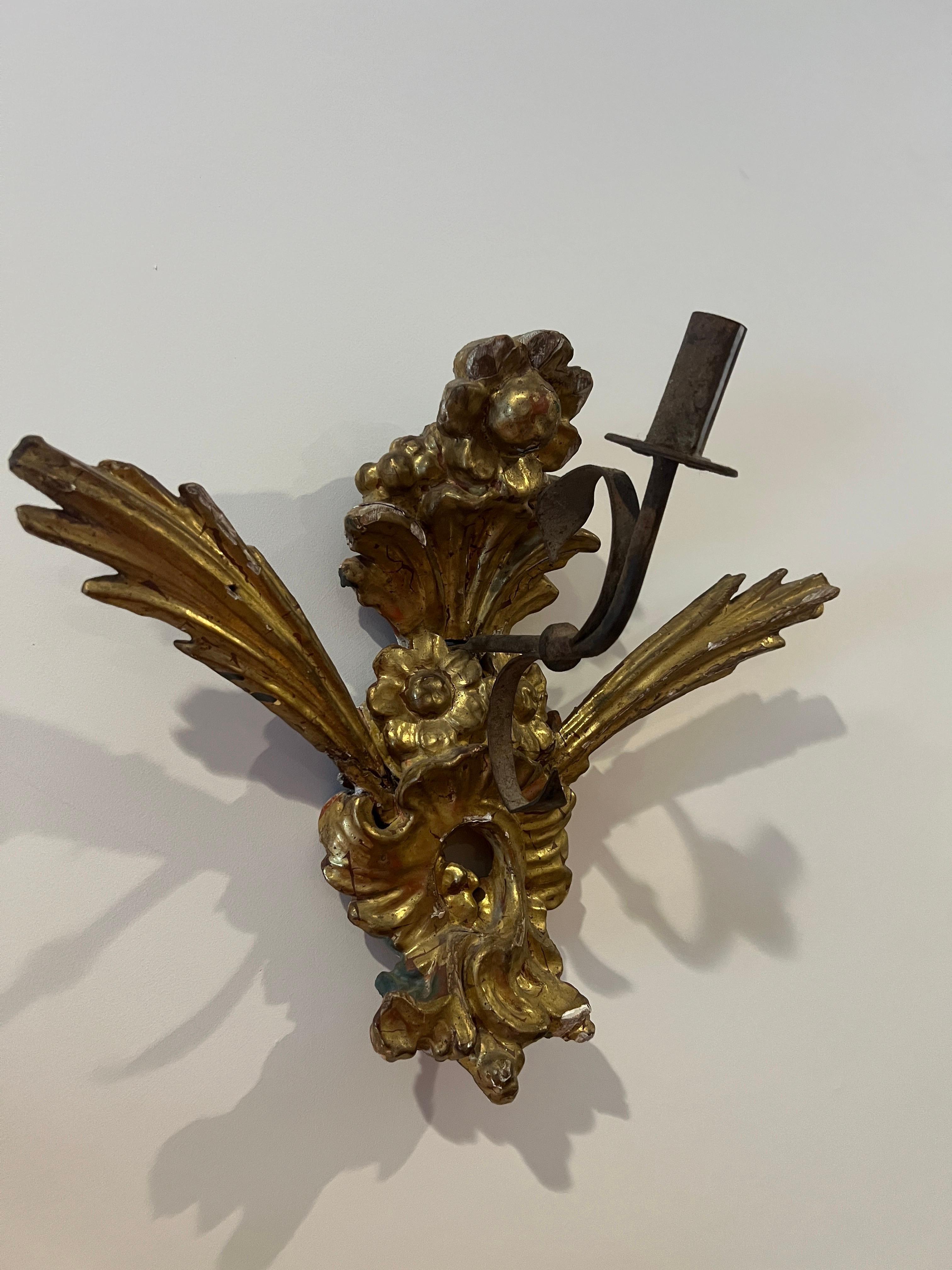 Italian, 18th century.

A good quality antique carved and water gilded single arm sconce. Featuring a Rococo and Renaissance Revival style - the sconce has a single hand forged wrought iron arm for a single candle. Likely from a church or religious