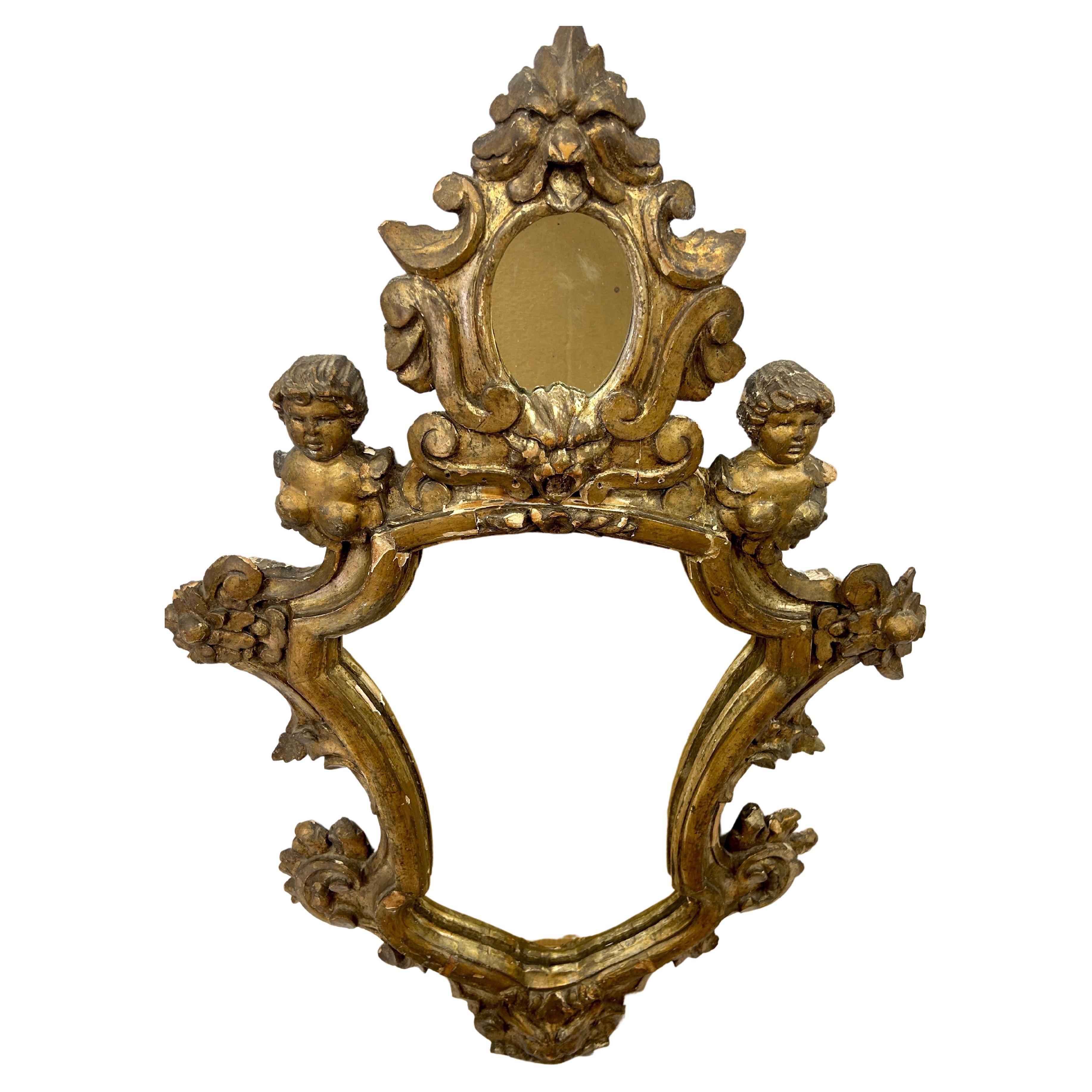 Large Italian baroque style giltwood wall mirror with cherubs and foliate carved surround. Has small oval mirror surrounded by intricate carved giltwood atop a larger mirror with gilt floral carving terminating into giltwood animal face.