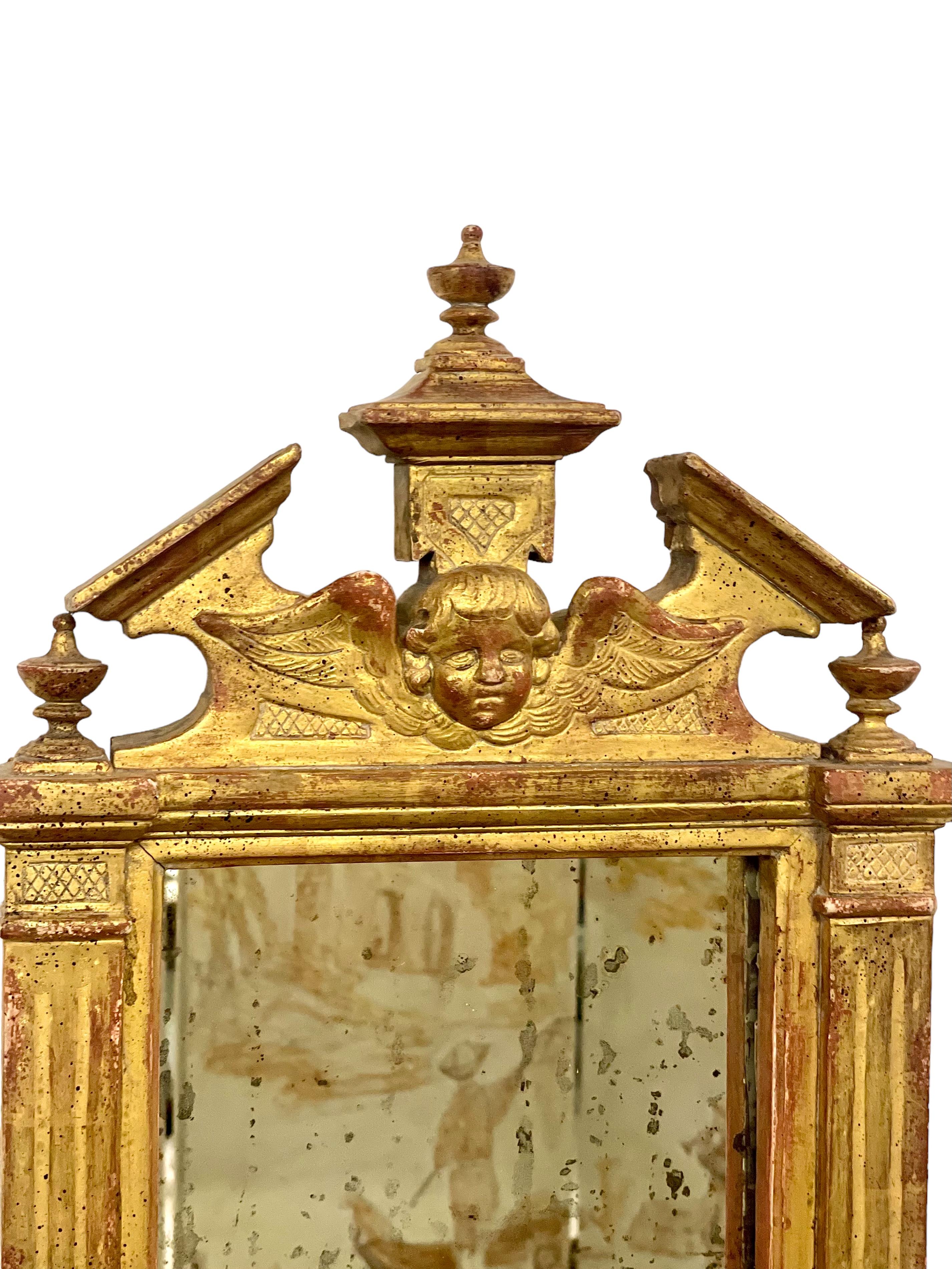 A late 18th-century Neoclassical wall mirror in the Baroque style, and originating from Italy. Beautifully carved, its giltwood frame features a triangular pediment, centred with a winged cherub flanked and topped by three miniature cassolettes.