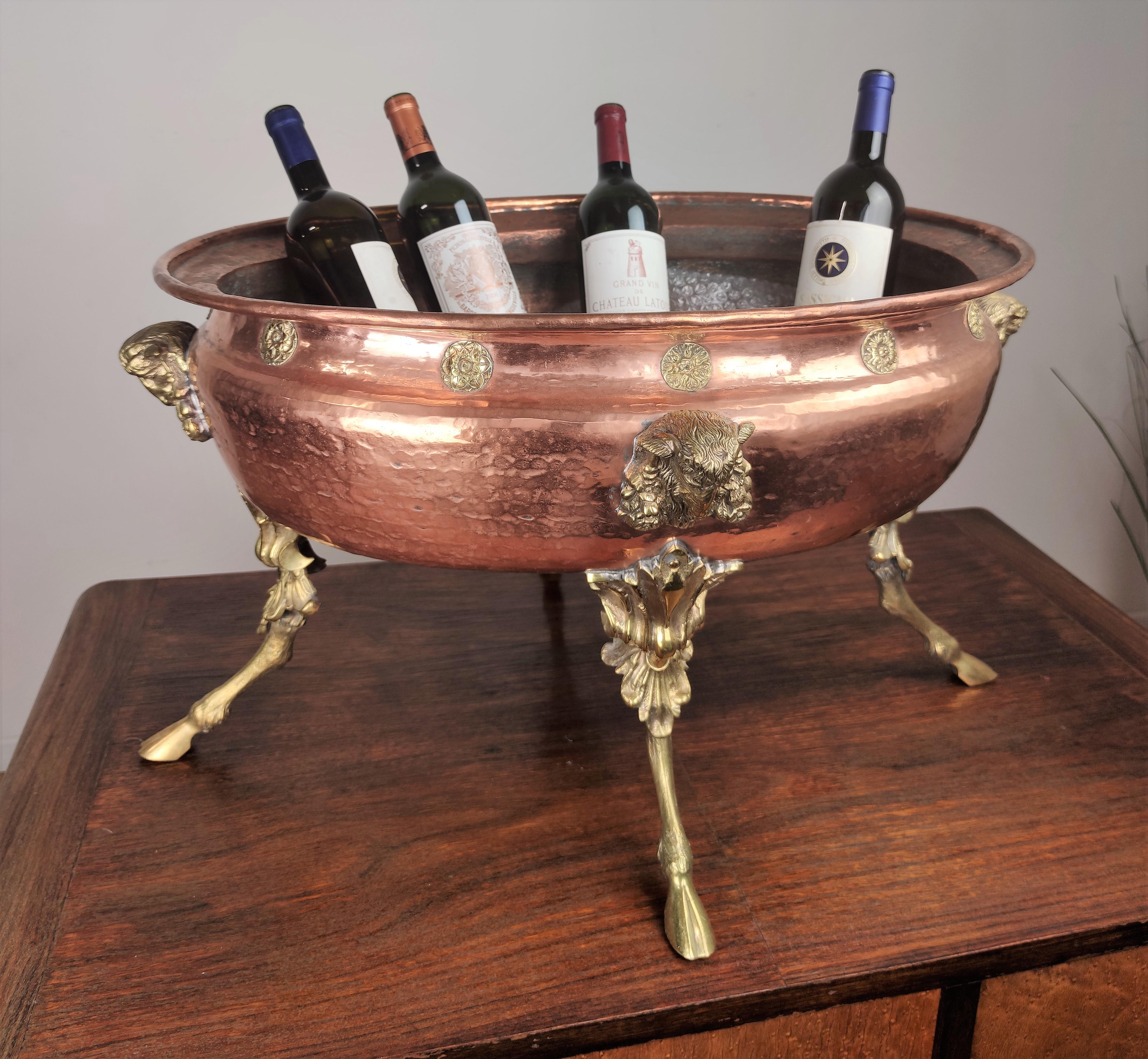 Beautiful, elegant and unique ice holder champagne wine cooler with its large bellied oval copper body fitted with rivet-mounted cast brass decors, figures & handles, and raised upon four carved feet. At the four sides we find four ram's heads