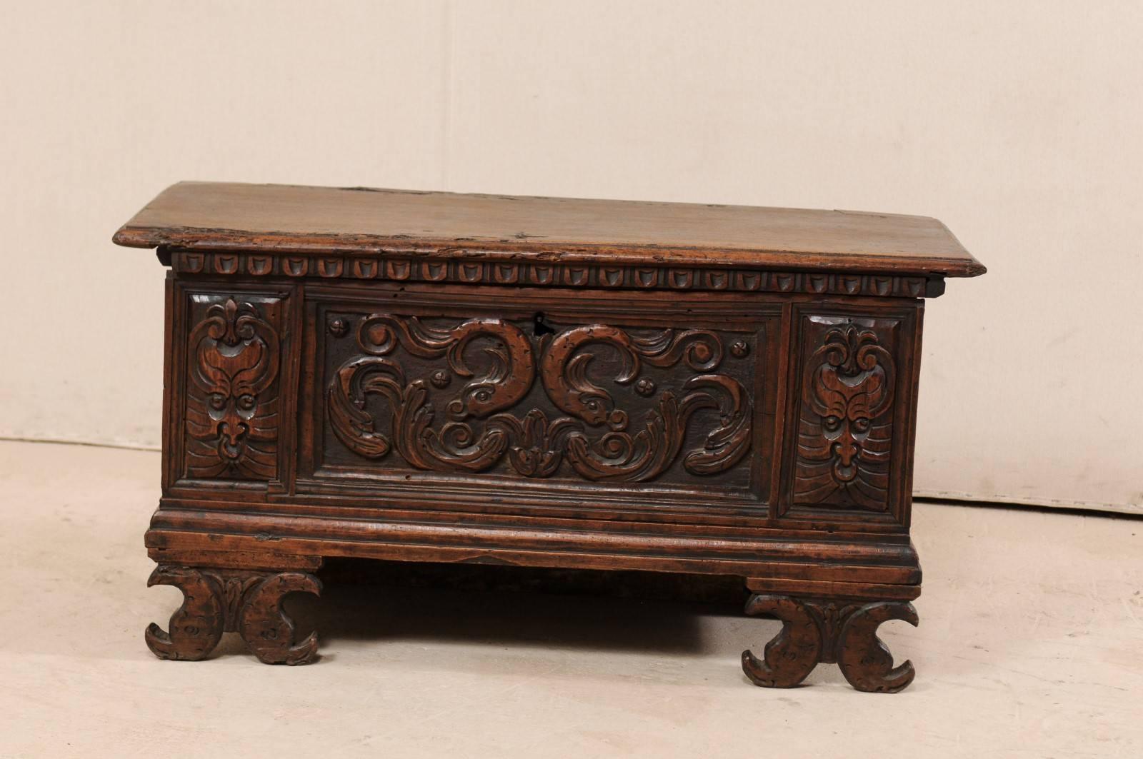 An Italian late 18th century carved wood cassone trunk. This antique cassone from Italy features an ornately hand-carved front center panel with mythical sea creatures flanked by a pair of faces set into front, side panels. This rectangular shaped