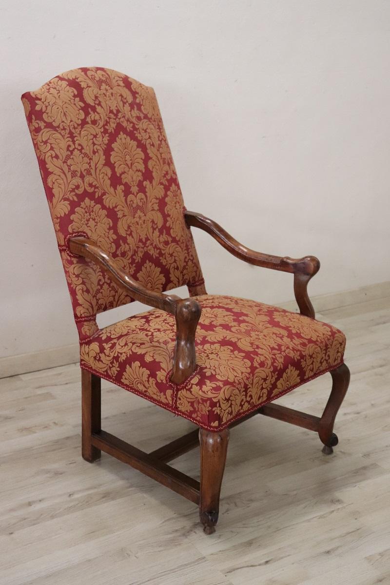 Beautiful early 18th century of the period Louis XIV Italian antique armchair in solid walnut wood. An imposing large armchair with a wide and comfortable seat. Wavy armrests and arched legs joined by a cross. Beautiful purple-red fabric with damask