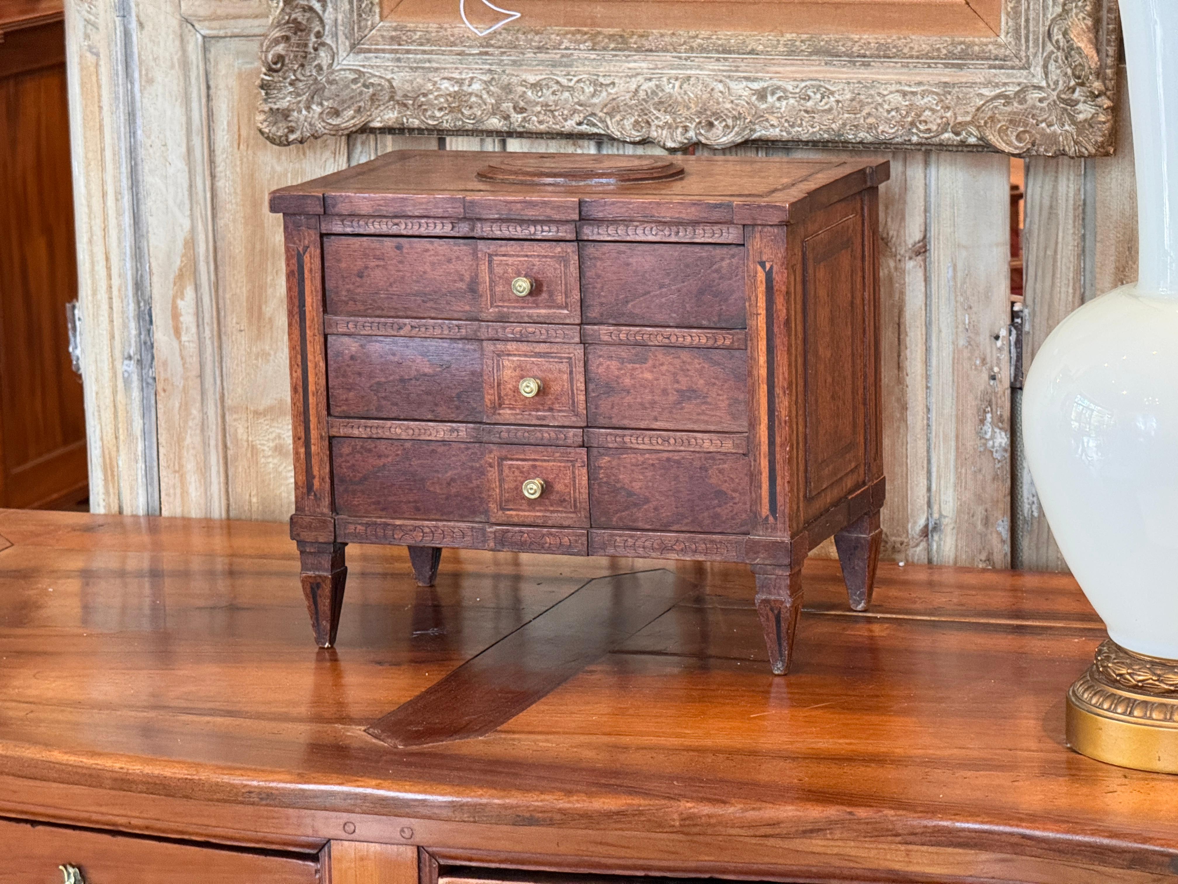Commodo italiano in miniatura del XVIII secolo con tre cassetti, tiranti in ottone e dettagli finemente intagliati e intarsiati. Le gambe affusolate e le proporzioni equilibrate riflettono il raffinato artigianato neoclassico dell'epoca.