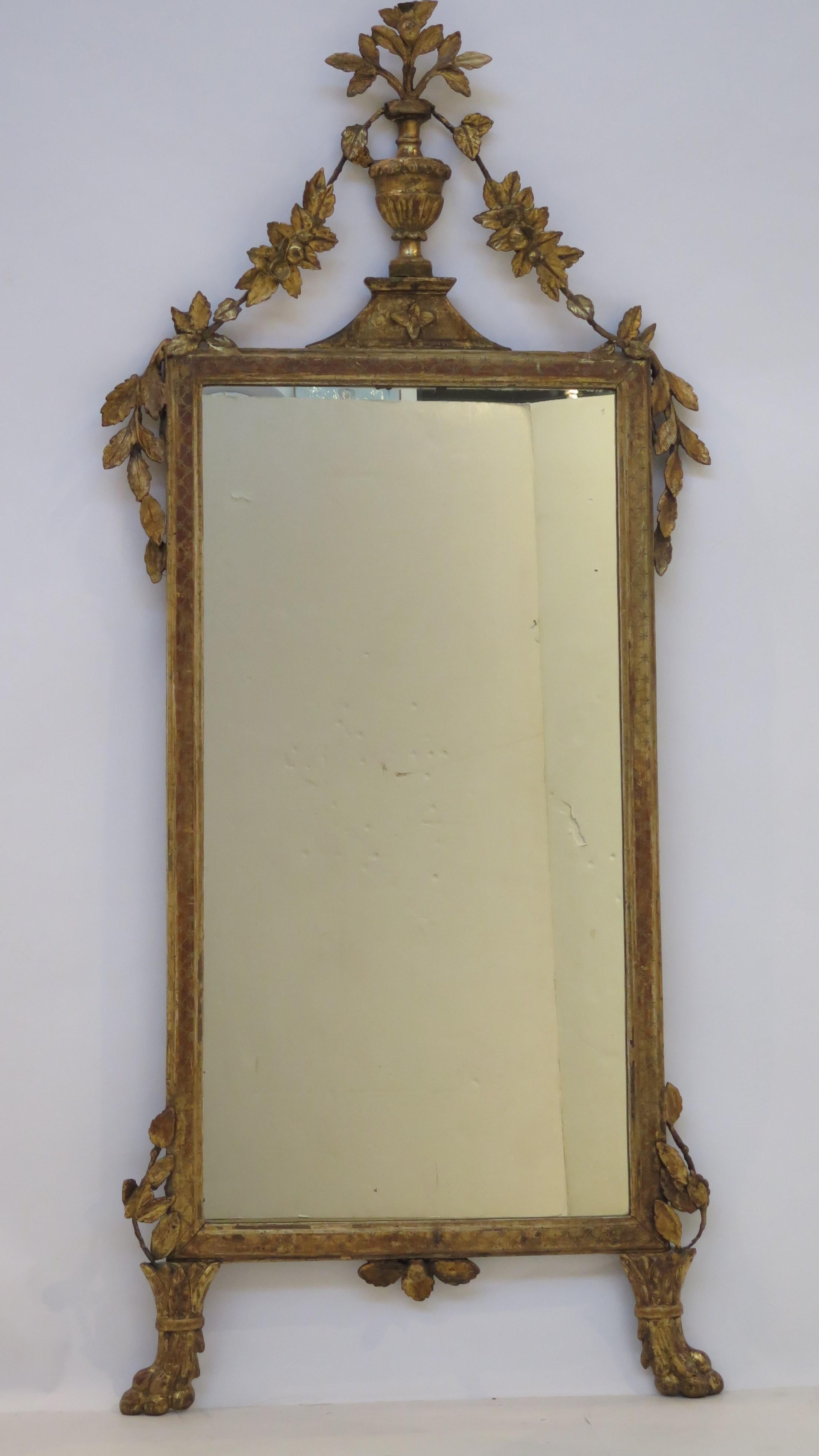 An Italian neoclassical carved and giltwood mirror. This rectangular form mirror features an urn with flowers at top, and floral swags at sides with cascading leaves accented by paw feet at the base.