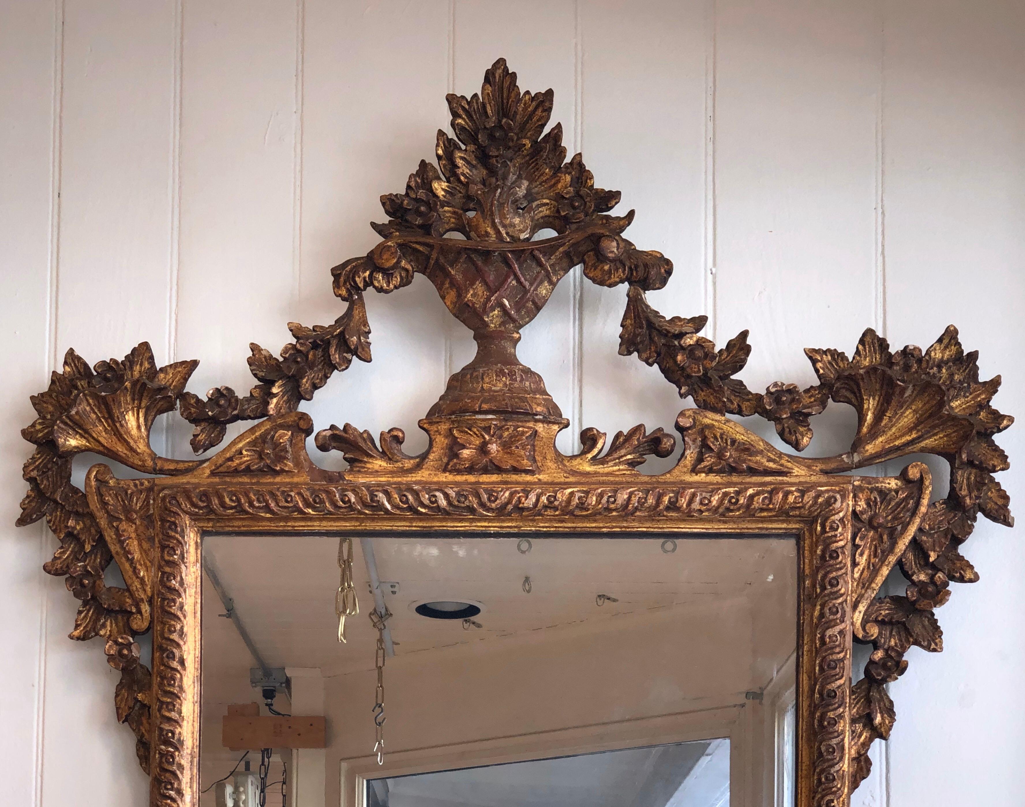This 1790s neoclassical intricately craved giltwood pier mirror is crowned with a foliate design urn having delicate garland swags flowing to the Cornucopia corners and hanging down the sides. The looking glass is surrounded by an Ancient Greek Wave