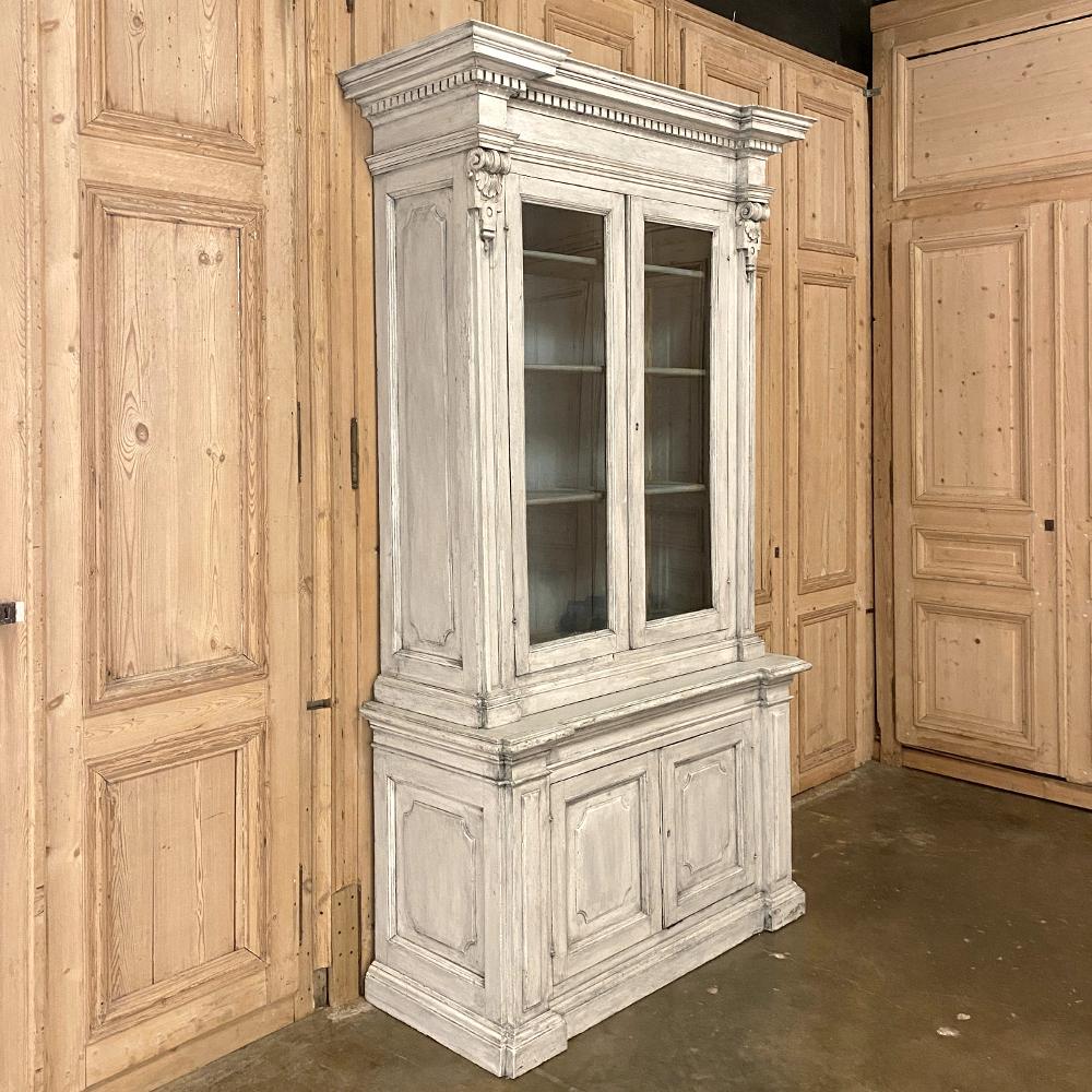18th century Italian neoclassical painted bookcase is a marvel of architecture inspired by the masters of ancient Greece and Rome! The boldly molded crown transitions to dentil trim above the bonnet, which overlooks the elongated glazed doors of the