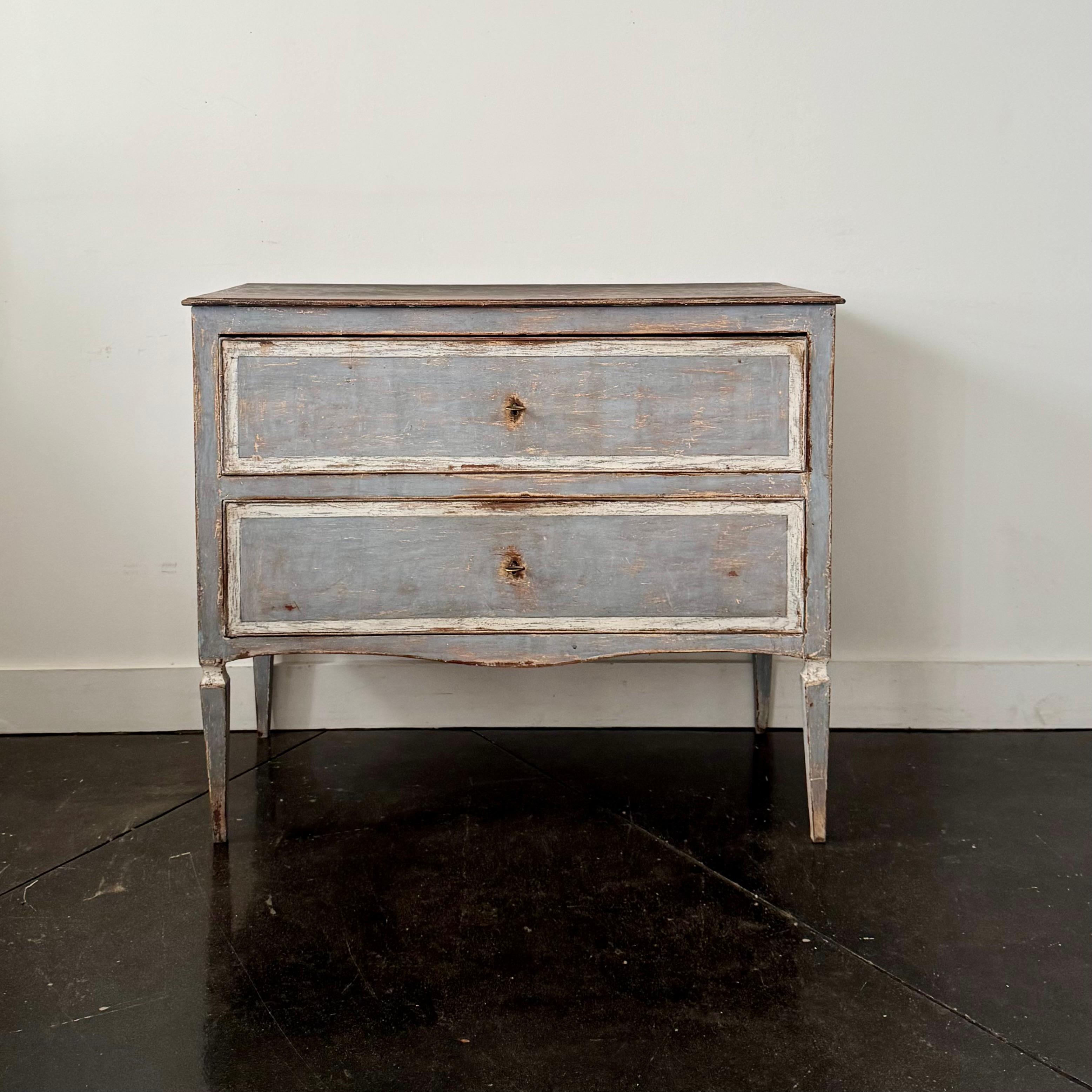 Charmante commode peinte de style néoclassique italien du XVIIIe siècle comprenant deux longs tiroirs avec garnitures décoratives blanches, reposant sur des pieds carrés effilés, qui confèrent à sa silhouette gracieuse une élégance intemporelle.