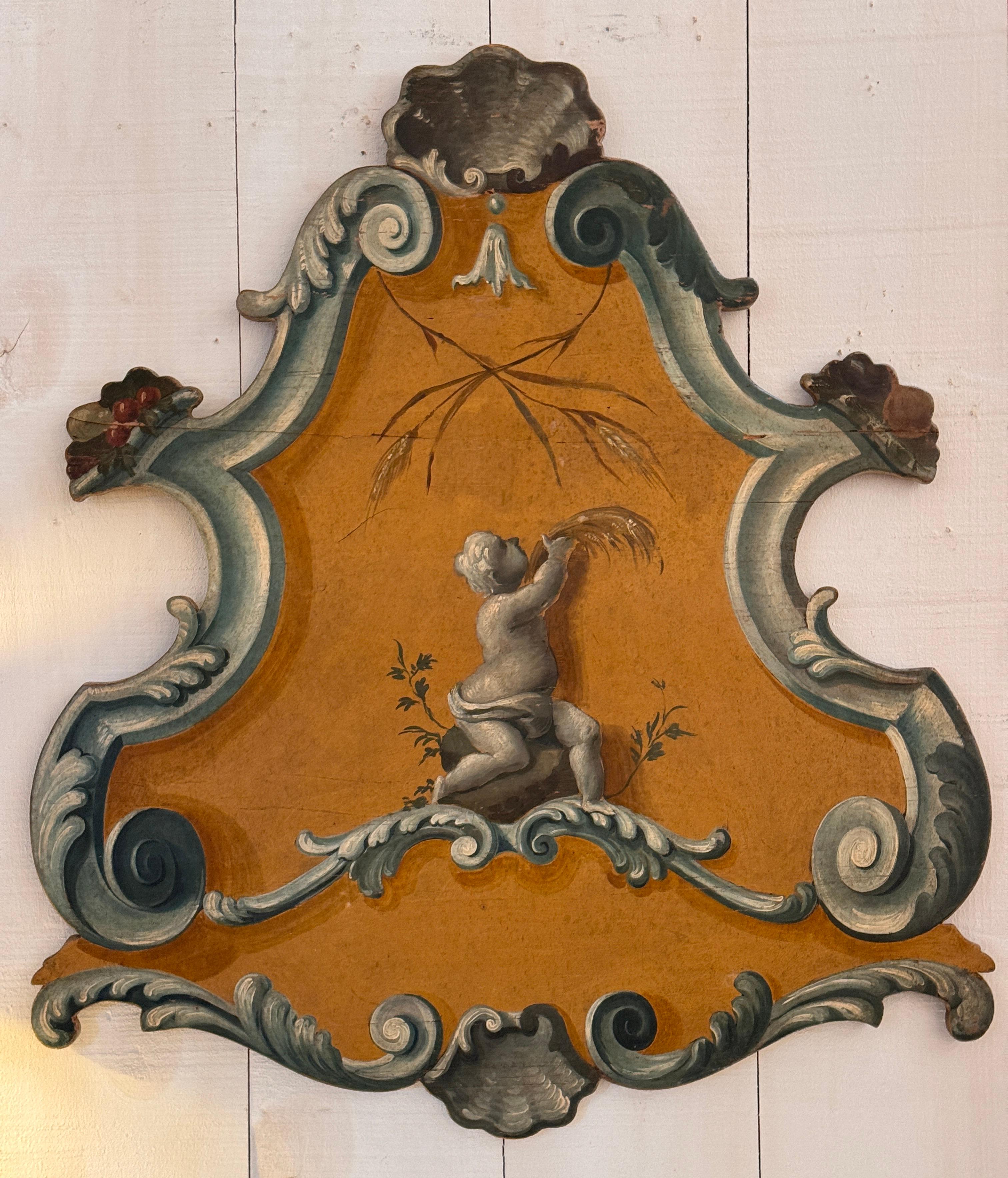 A vibrant 18th century Italian rococo panel with shaped silhouette, painted in ochre and celadon tones. The central figure—a cherubic child gathering wheat—is framed by ornate scrollwork and stylized shell motifs. A decorative fragment that reflects