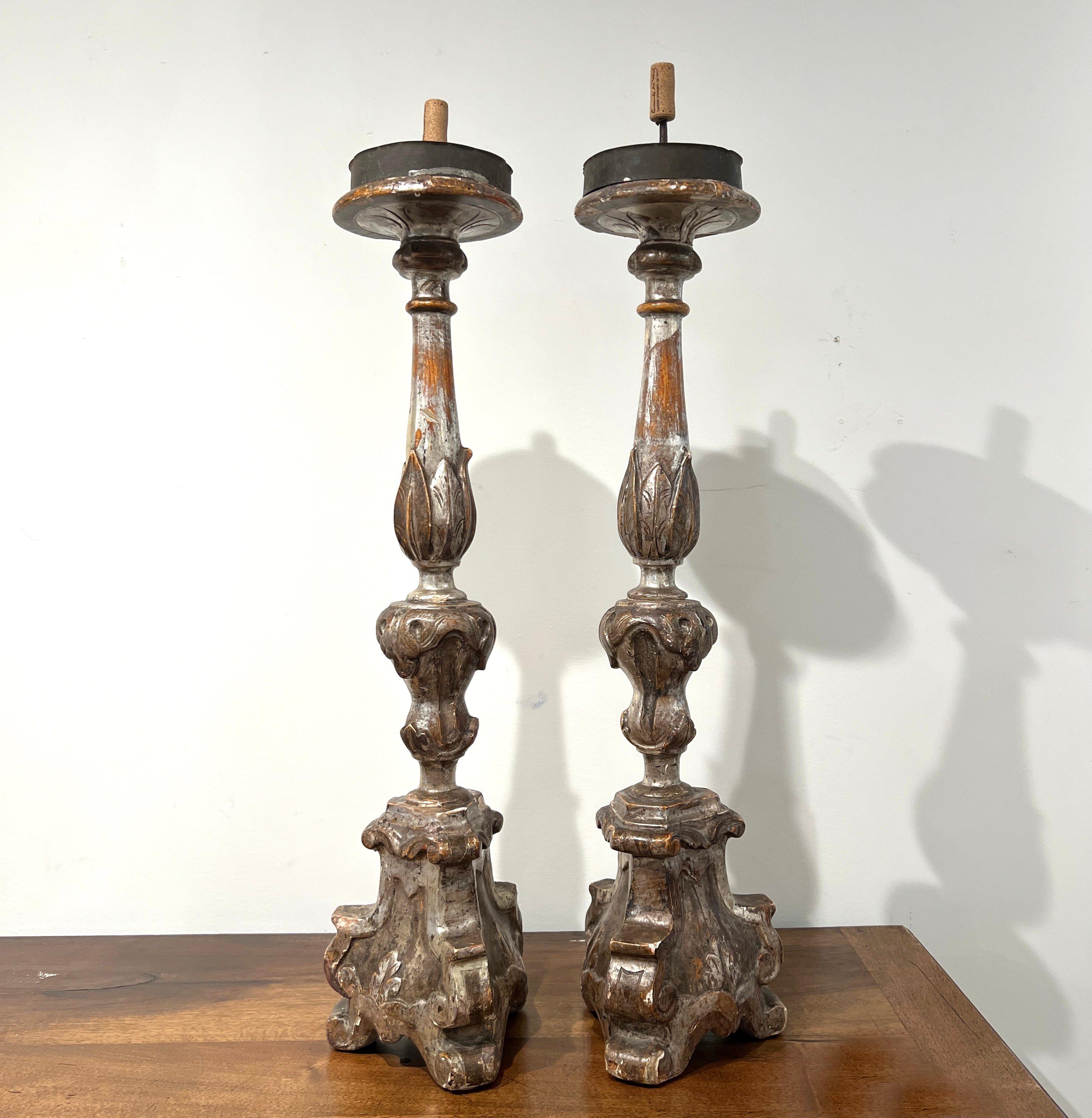 Une paire de chandeliers baroques ornés de feuilles d'argent lumineuses, de volutes audacieusement sculptées, de détails d'acanthe et de courbes spectaculaires, qui illustrent l'élégance théâtrale du design du XVIIe siècle.