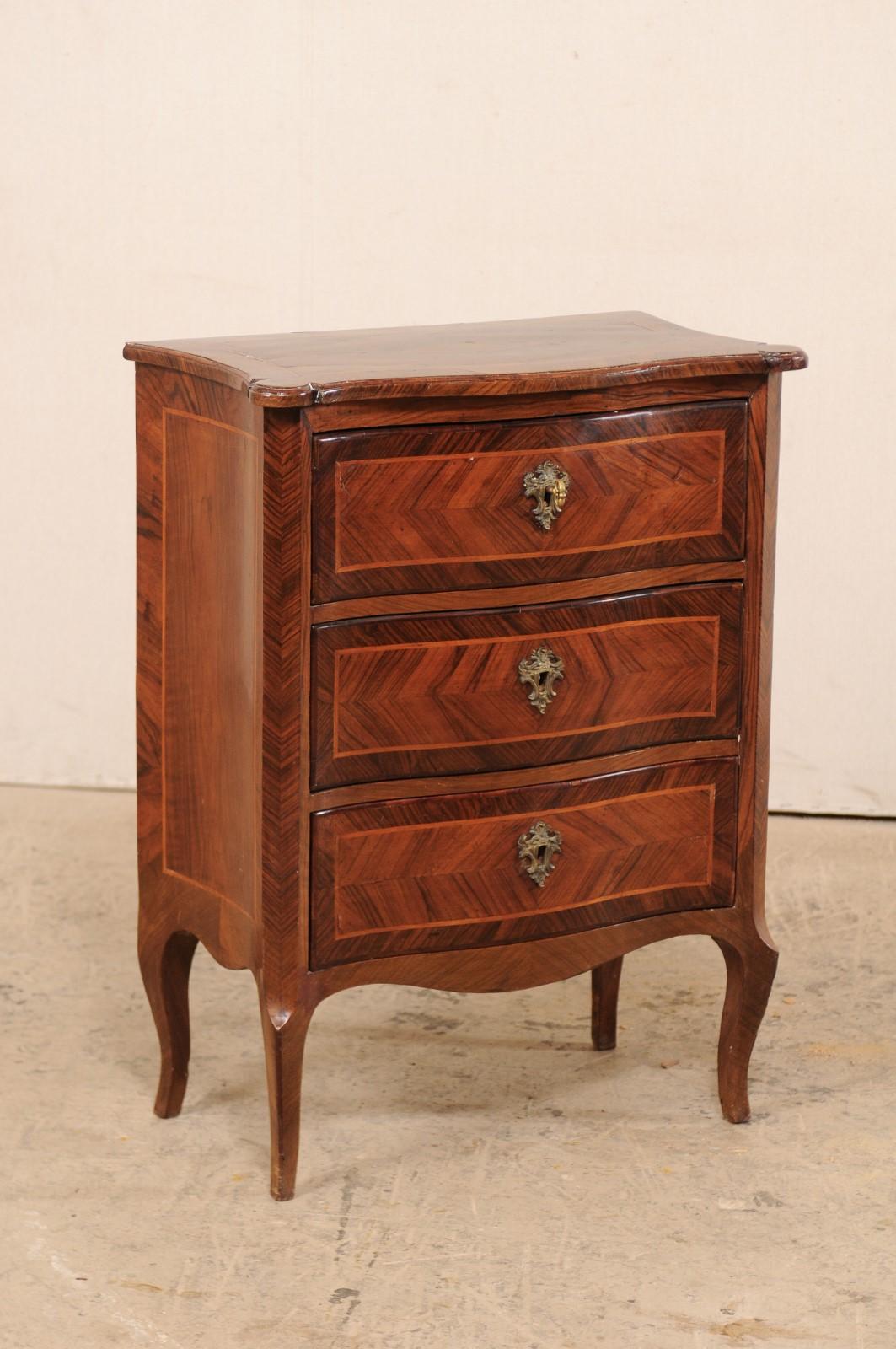 A small-sized Italian side chest of three drawers from the 18th century. This antique commode from Italy features beautiful banding and inlay details within a shapely body with subtly bowed front and concave sides. The top has a simple yet elegant