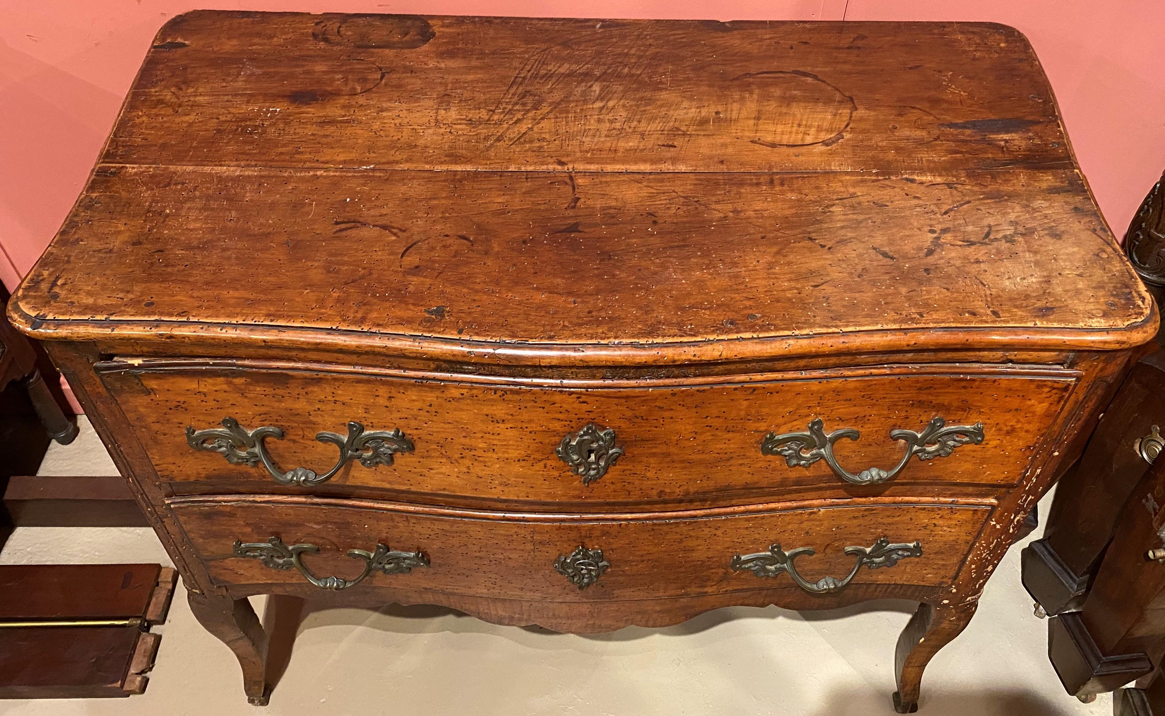 A fine Italian, probably Venetian walnut two drawer commode with a subtle serpentine front, conforming molded edge top, foliate period brasses, nicely shaped skirt, and great patina. The commode dates to the 18th century and is in good overall
