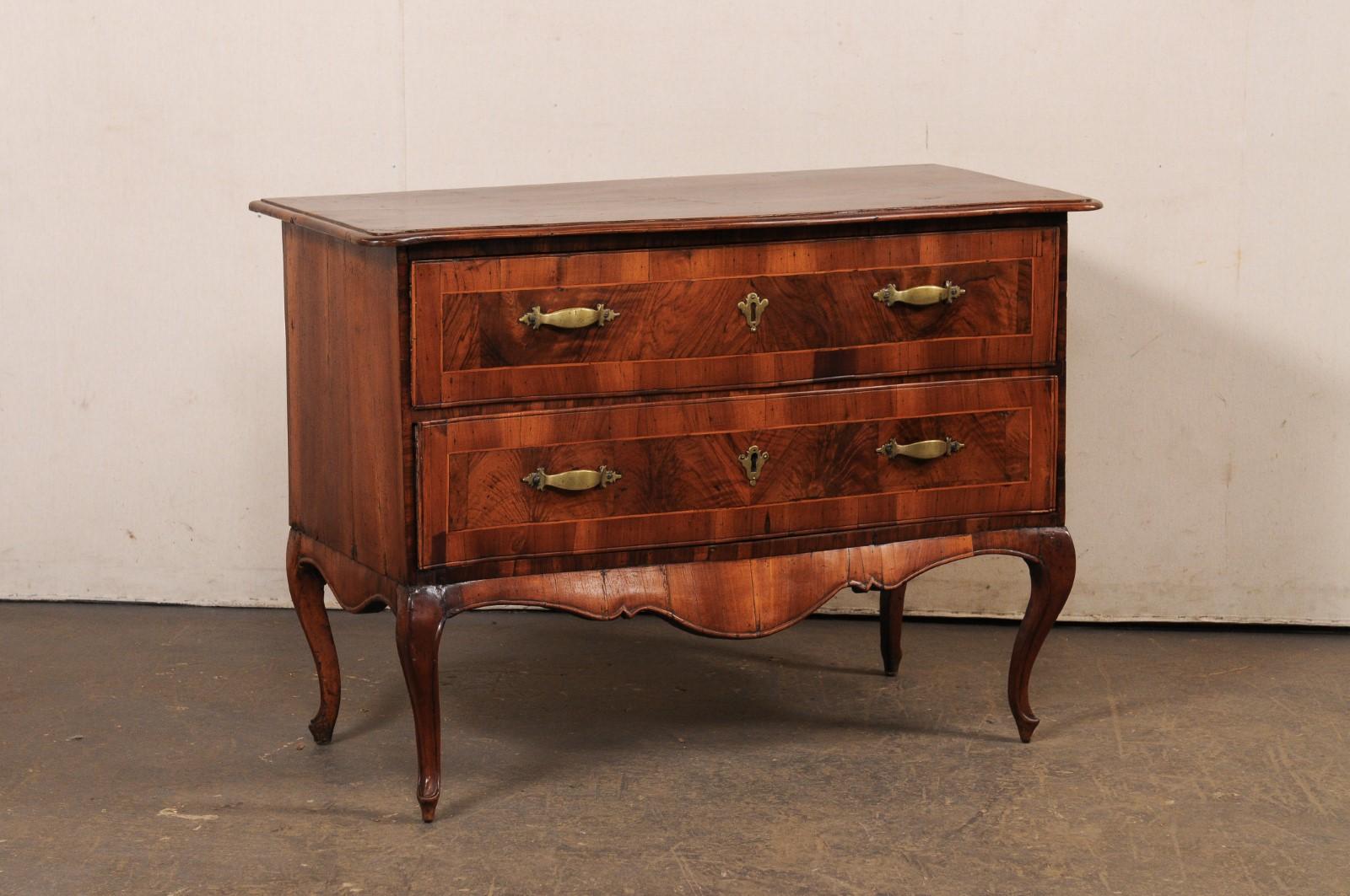 An Italian raised two-drawer chest, with decorative inlay and brass hardware, from the 18th century. This antique cassettiera (chest of drawers) from Italy features a rectangular-shaped top with front having a serpentine shape, which continues down