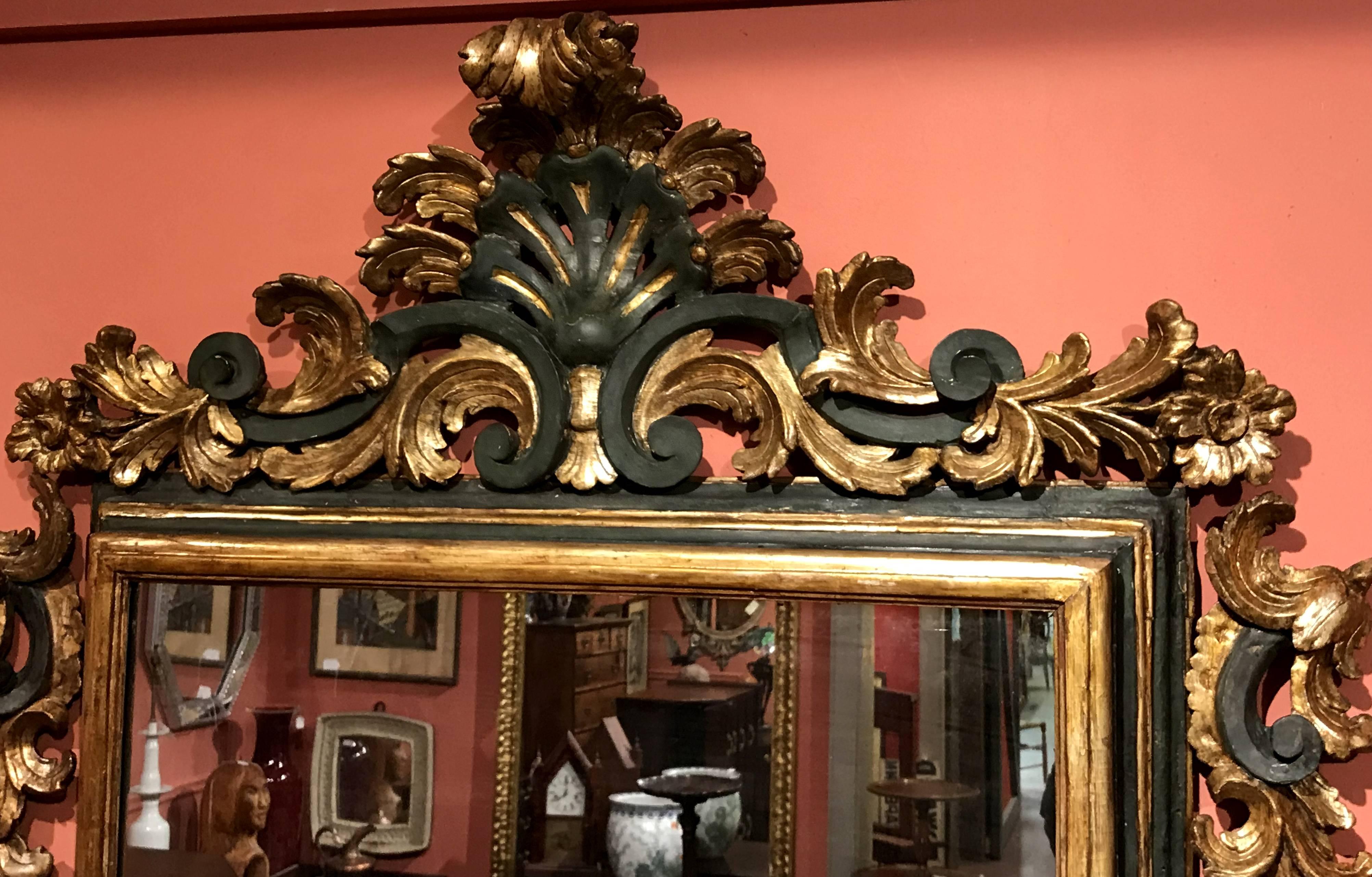 A fine Rococo wall mirror with polychrome and gilt molded wooden frame, highlighted with an exceptional foliate and scroll carved crest and surround. Italian, dating to the mid 18th century, in fine overall condition, with restorations and