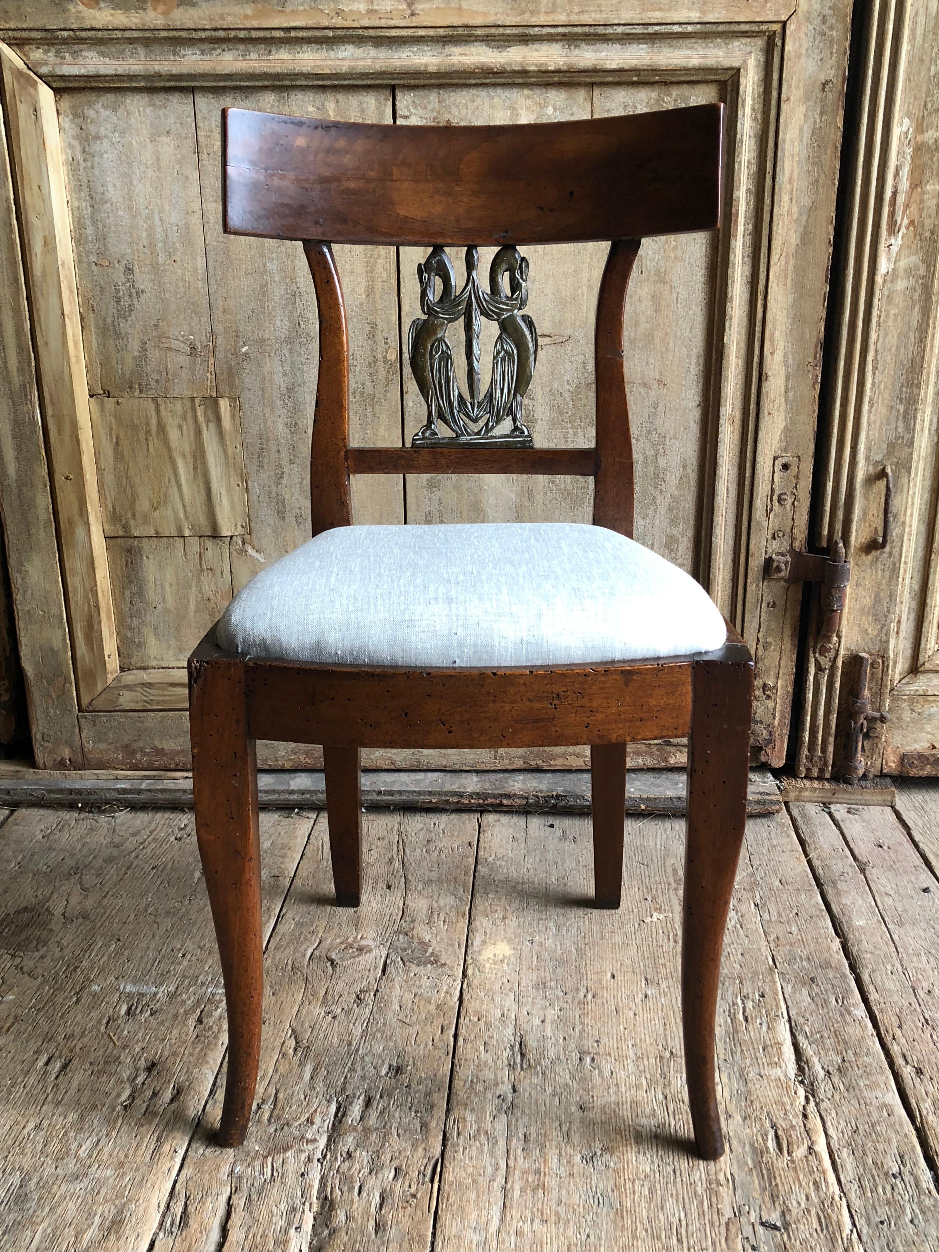 An 18th century Italian side chair in walnut with a “yoke-back” and an inset carved back panel with 2 winged griffons, the panel showing some traces of old paint, over a slip seat recovered in grey linen all on simple splayed legs, circa 1780.