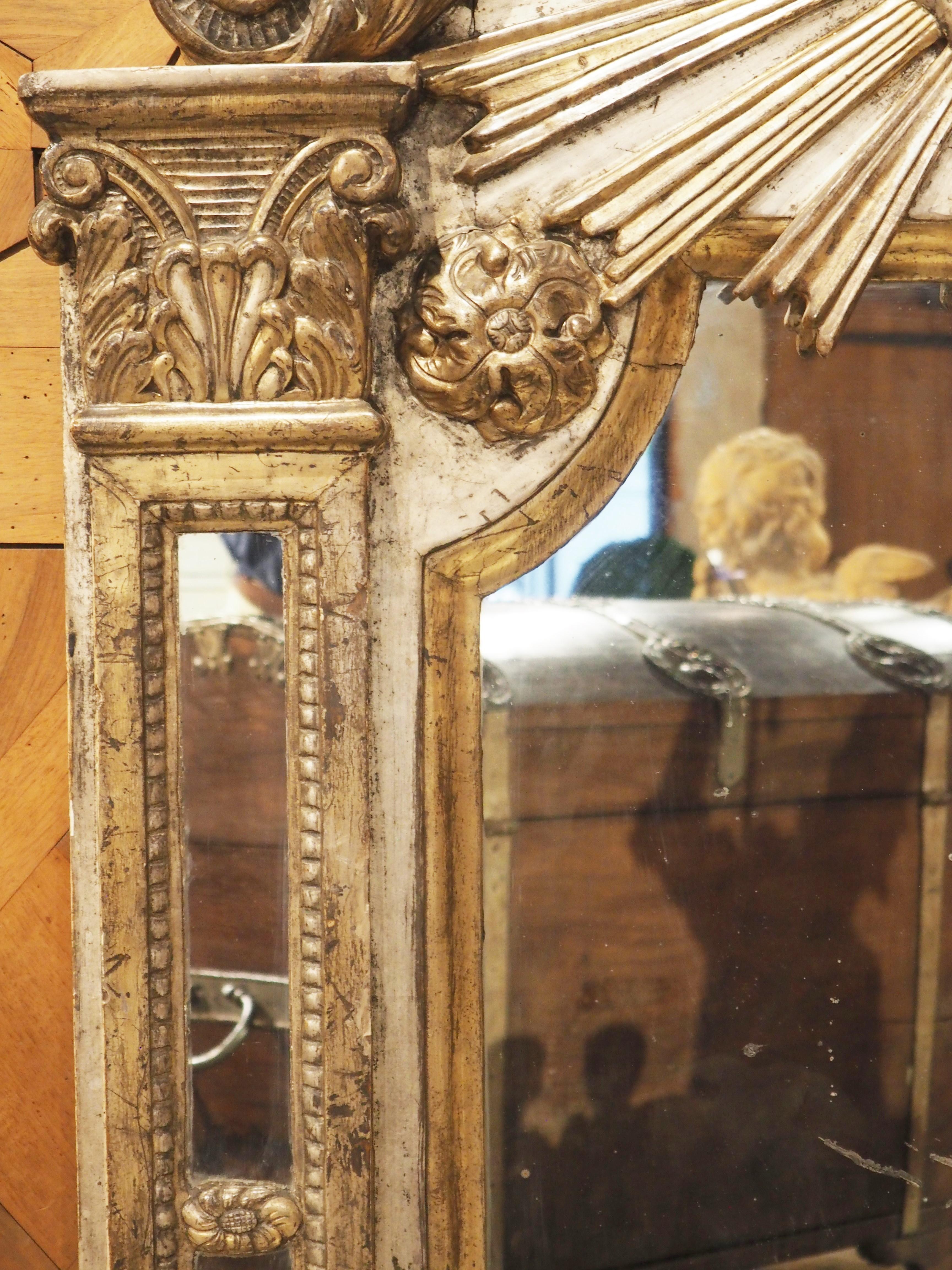 Hand-carved in Italy in the 1700’s, this silvered and giltwood parecloses mirror has a large sunburst crest. The central sun is surrounded by a stylized circular cloud, with beams of light radiating from beneath it. Flanking the crest is a pair of