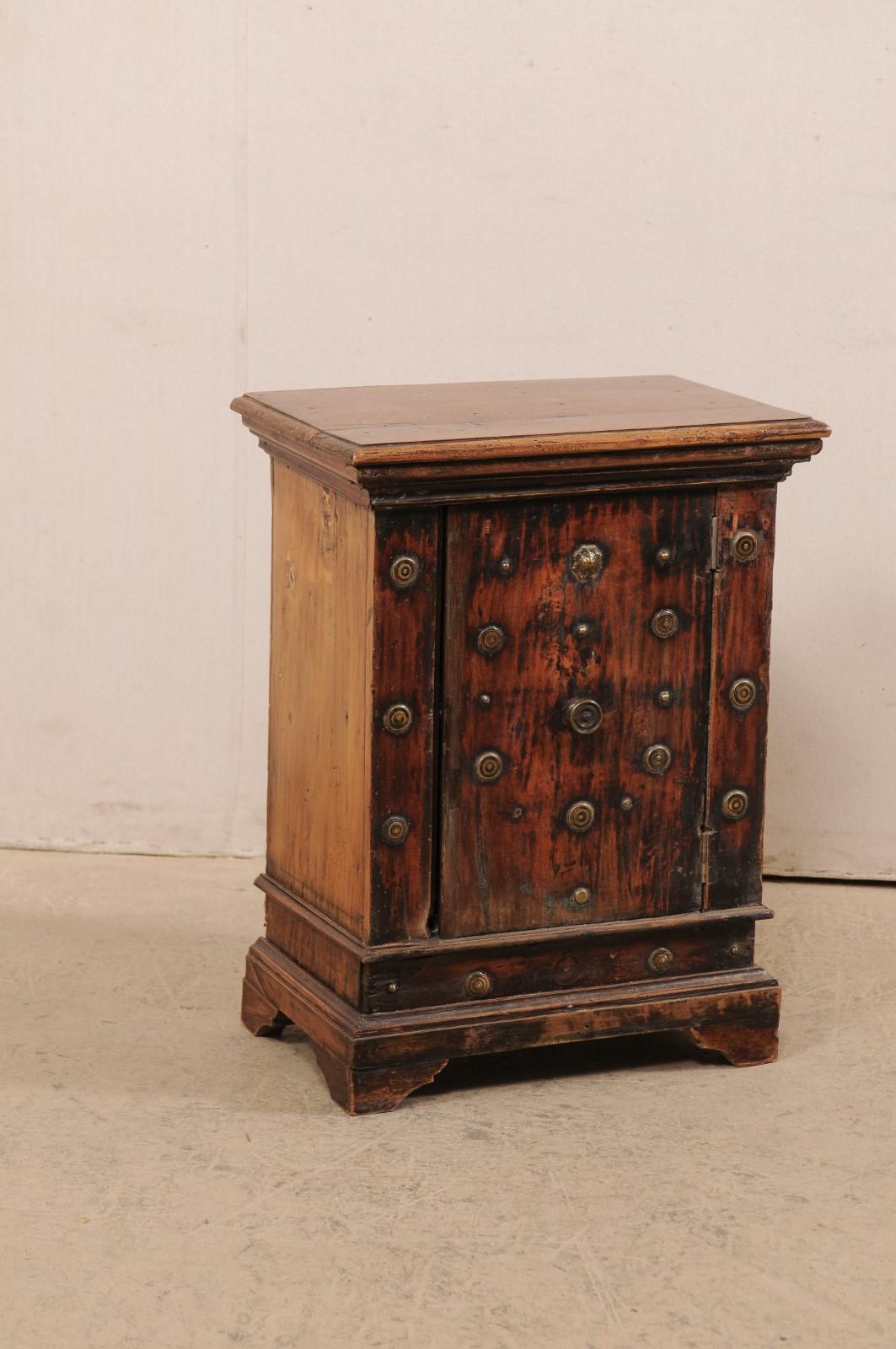 An Italian small-sized wooden cabinet with brass accents from the 18th century. This antique side cabinet from Italy is beautifully decorated in numerous brass medallions about it's front side. The rectangular-shaped top is stack-molded, resting