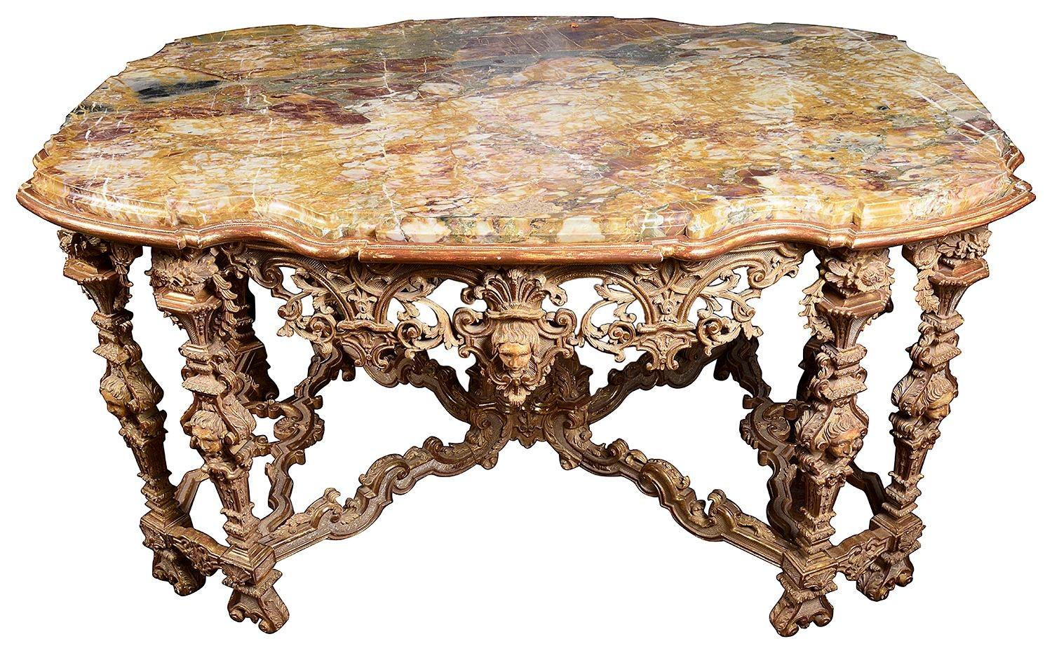 Splendido tavolo da centro in legno dorato intagliato a mano del XVIII secolo, con piano in marmo di Siena, decorazione classica a volute traforate sul fregio, ciascuna delle otto gambe con maschere e decorazioni floreali, unite da una barella