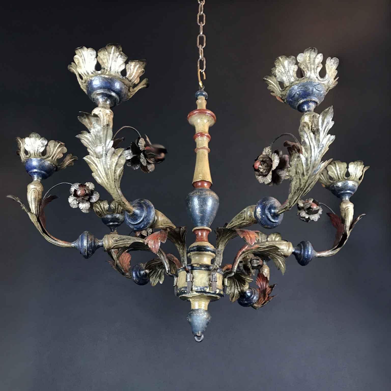 Antique fashinating circular chandelier realized for candle lighting, han-made in Italy in embossed leaf shaped iron tole with a central ivory, blue and red color painted wood stem decorated with six curved arms in embossed silver-leaf tole with red