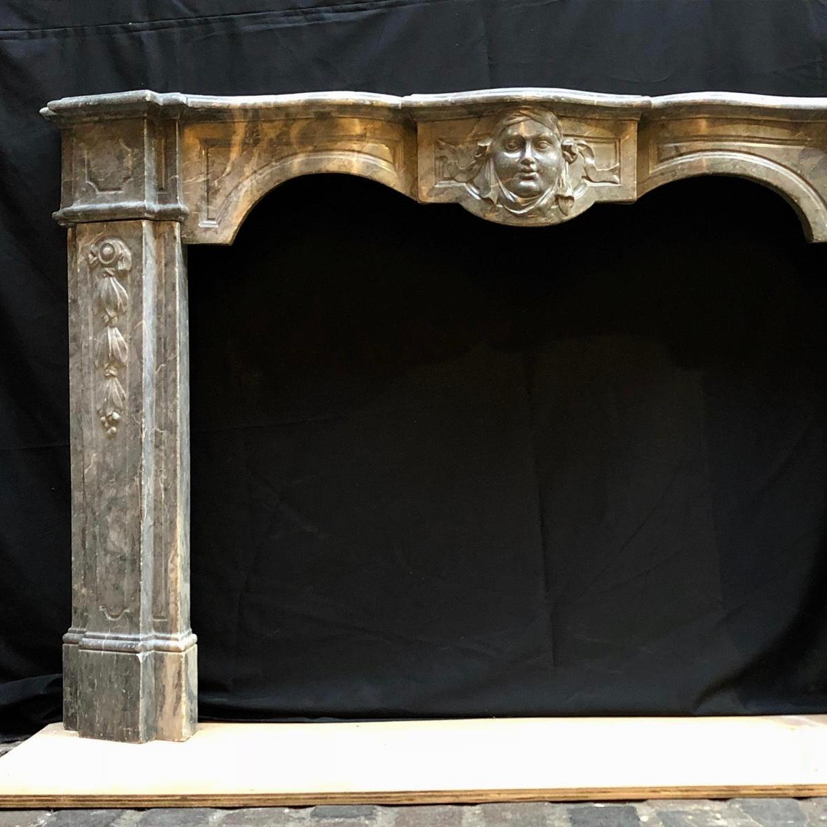 This stunning 18th century fireplace mantel is made from Bleu Turquin Marble. Made in Italy, this fireplace has a beautifully sculpted serpentine entablature with a centrally carved Mascaron. The jambs of this fireplace are decorated with leaves