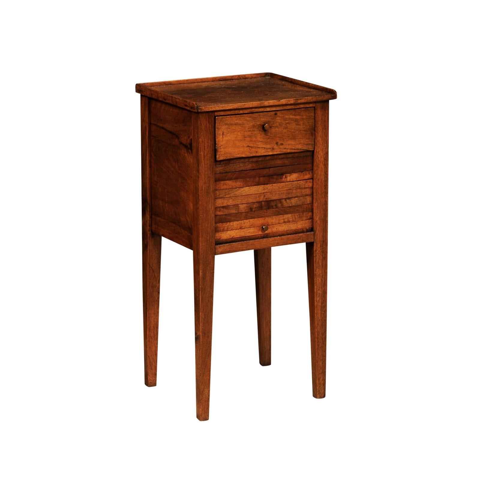 An Italian walnut bedside table from the 18th century with single drawer at the top, tambour door below and four tapered legs. Discover the rustic charm and functional elegance of this 18th-century Italian walnut bedside table, a piece that