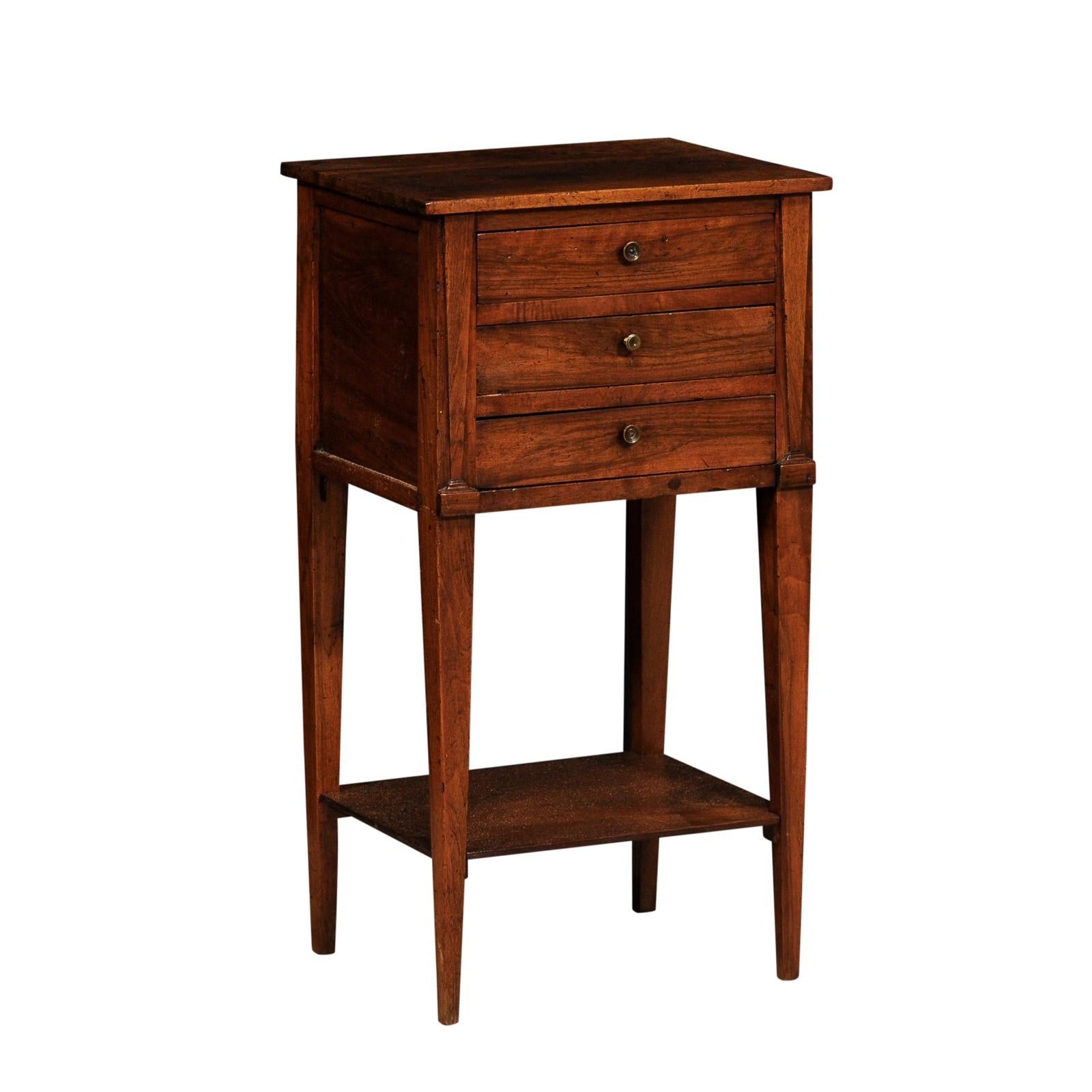 An Italian walnut bedside table from the 18th century with three drawers, lower shelf and tapering legs. Step back in time with this exquisite Italian walnut bedside table from the 18th century, a testament to the craftsmanship and artistry of the