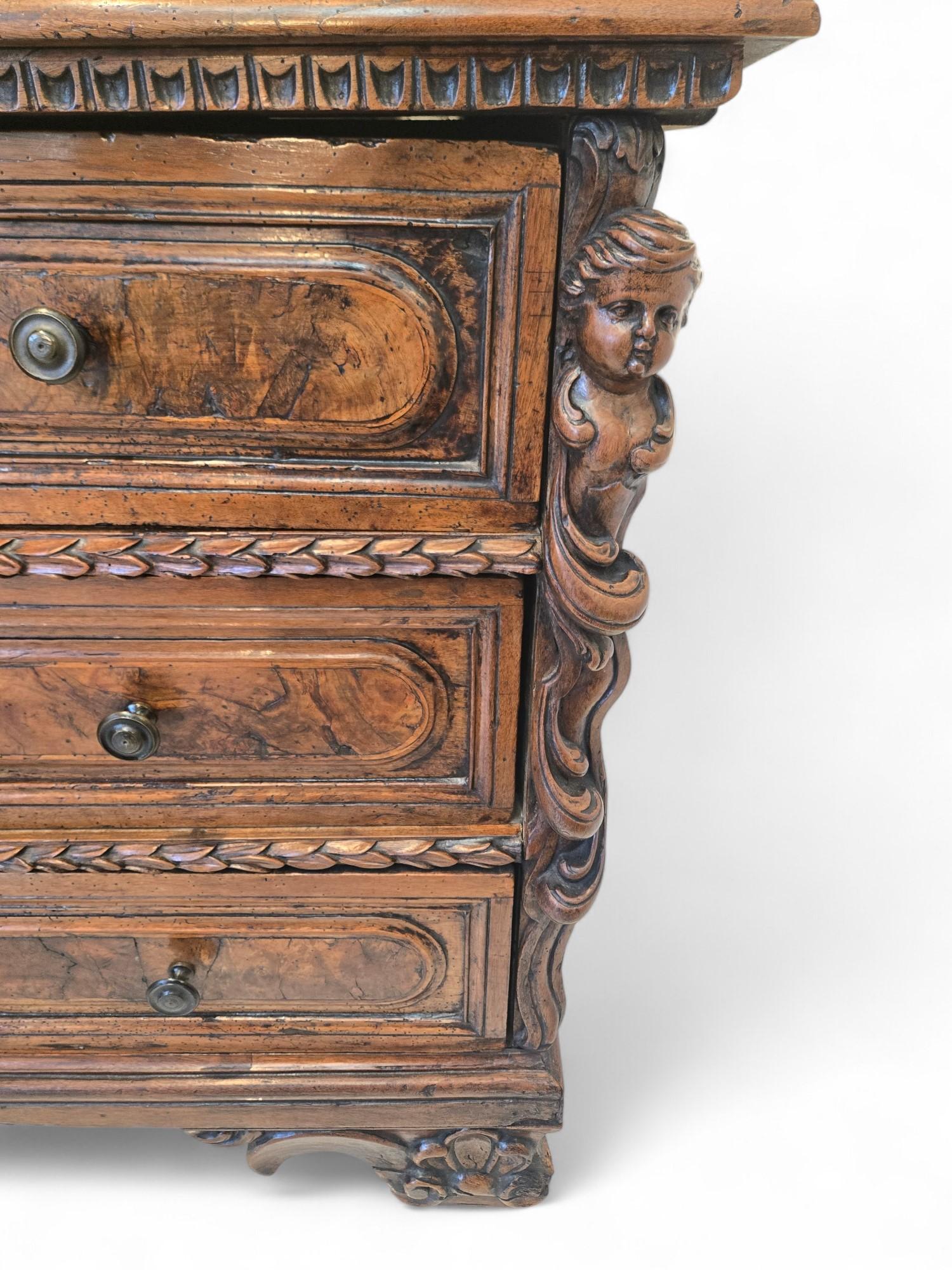 A magnificent Italian walnut commode, circa 1770, with richly carved detail and superb patina. This three-drawer chest features beautifully figured walnut panels framed with bold molding and stylized laurel leaf carving. The corners are flanked by