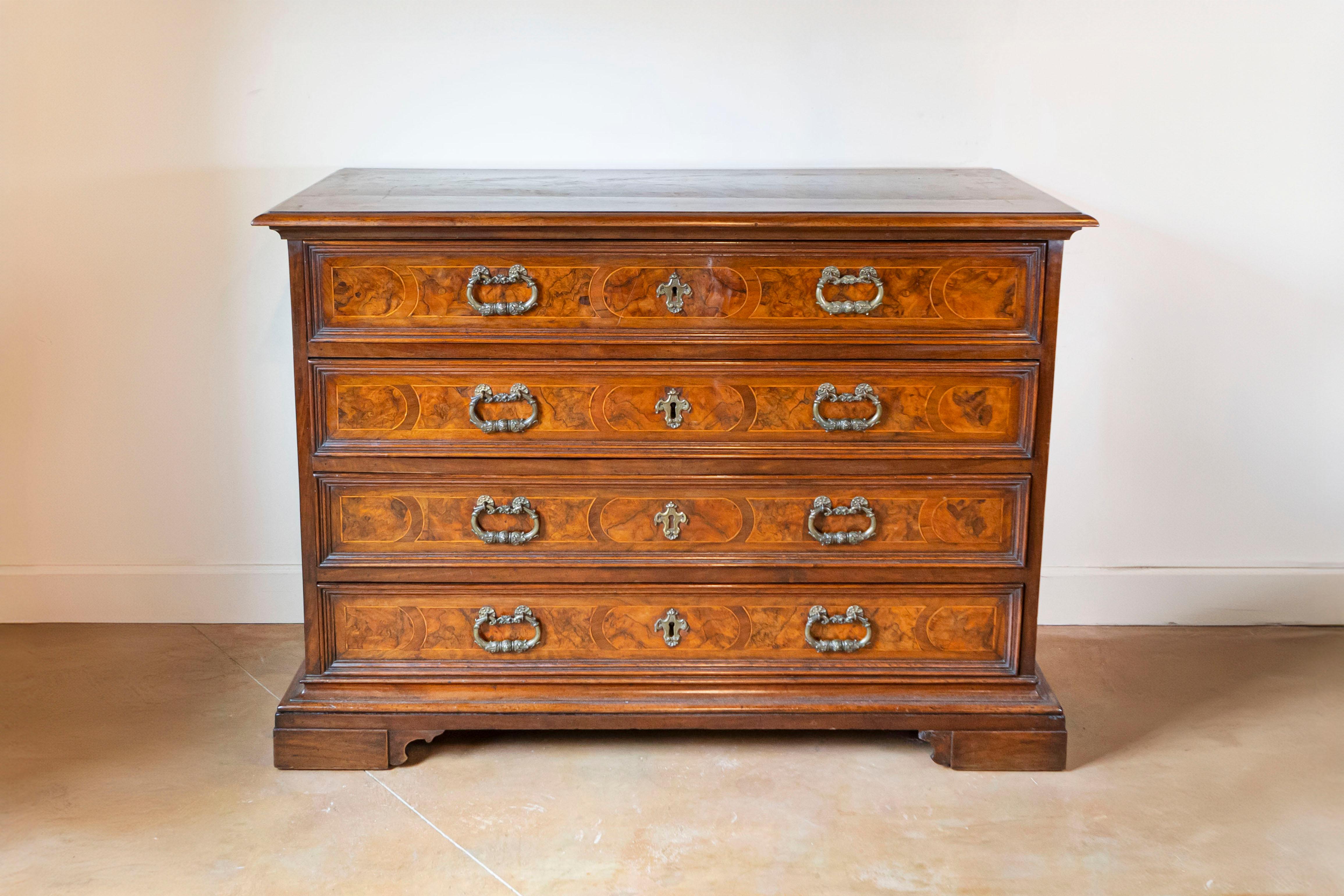 An Italian walnut commode from the 18th century with four drawers and carved bracket feet. Unveil an opulent slice of 18th-century Italy in your home with this spellbinding Italian walnut commode. Exuding an air of timeless grandeur, this