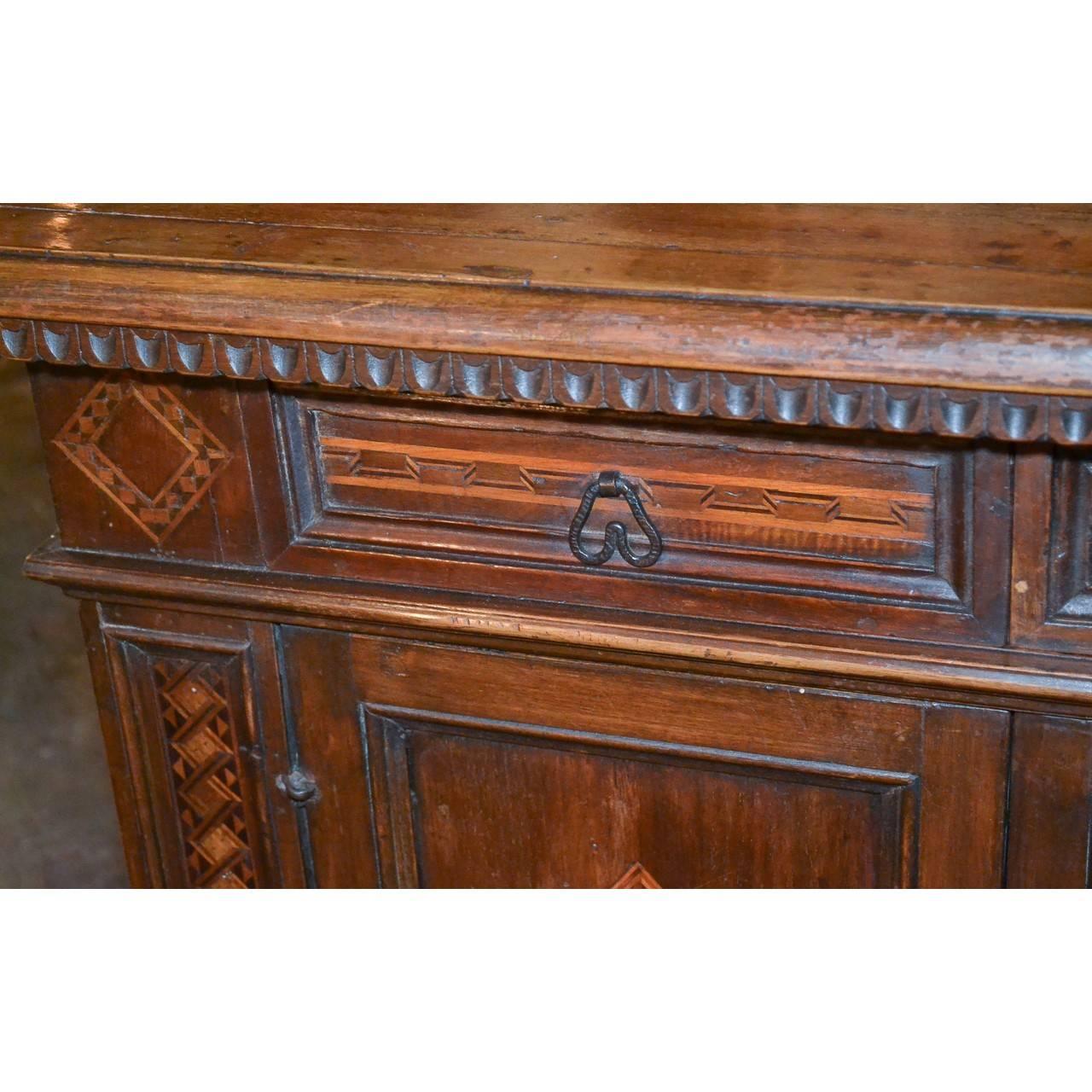 18th century Italian walnut side cabinet with finely aged patina. The frieze fitted with a single drawer having satinwood inlays atop a single cupboard with incised geometric carvings flanked by additional inlays. The entire on shaped bracket