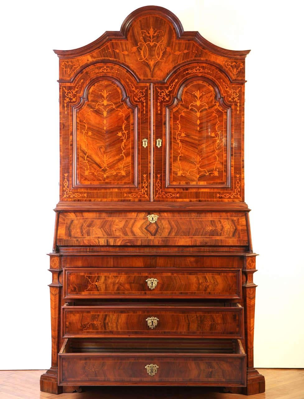 An Italian walnut, parquetry bureau cabinet fruitwood inlaid with scrolling foliage,
The upper section with a shaped carved cresting, a shaped doors opening to reveal three shelves, the lower section with a sloping-front,
Opening to reveal a