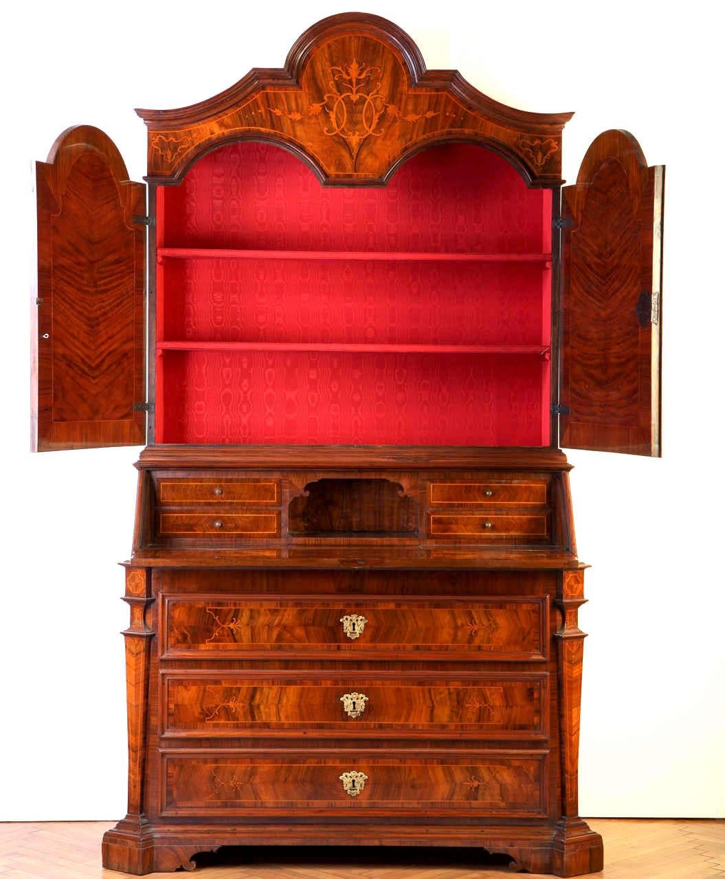 An Italian walnut, parquetry bureau cabinet fruitwood inlaid with scrolling foliage,
The upper section with a shaped carved cresting, a shaped doors opening to reveal three shelves, the lower section with a sloping-front,
Opening to reveal a