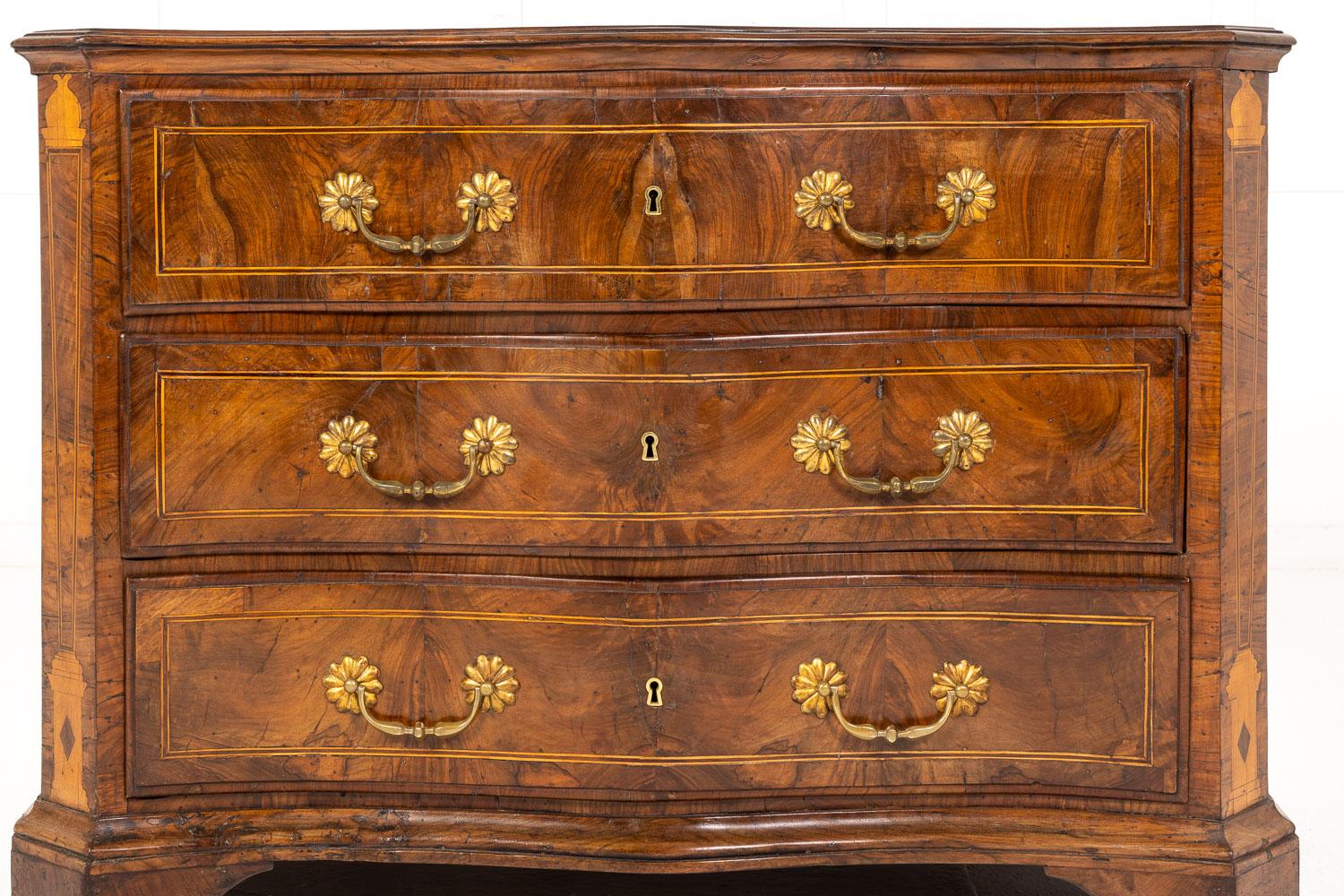 18th Century Italian serpentine commode constructed in walnut. Having a quarter veneered moulded and cross banded top with fine stringing/inlay conforming to the shape below. Three generous sized, deep drawers, with large drop brass handles are