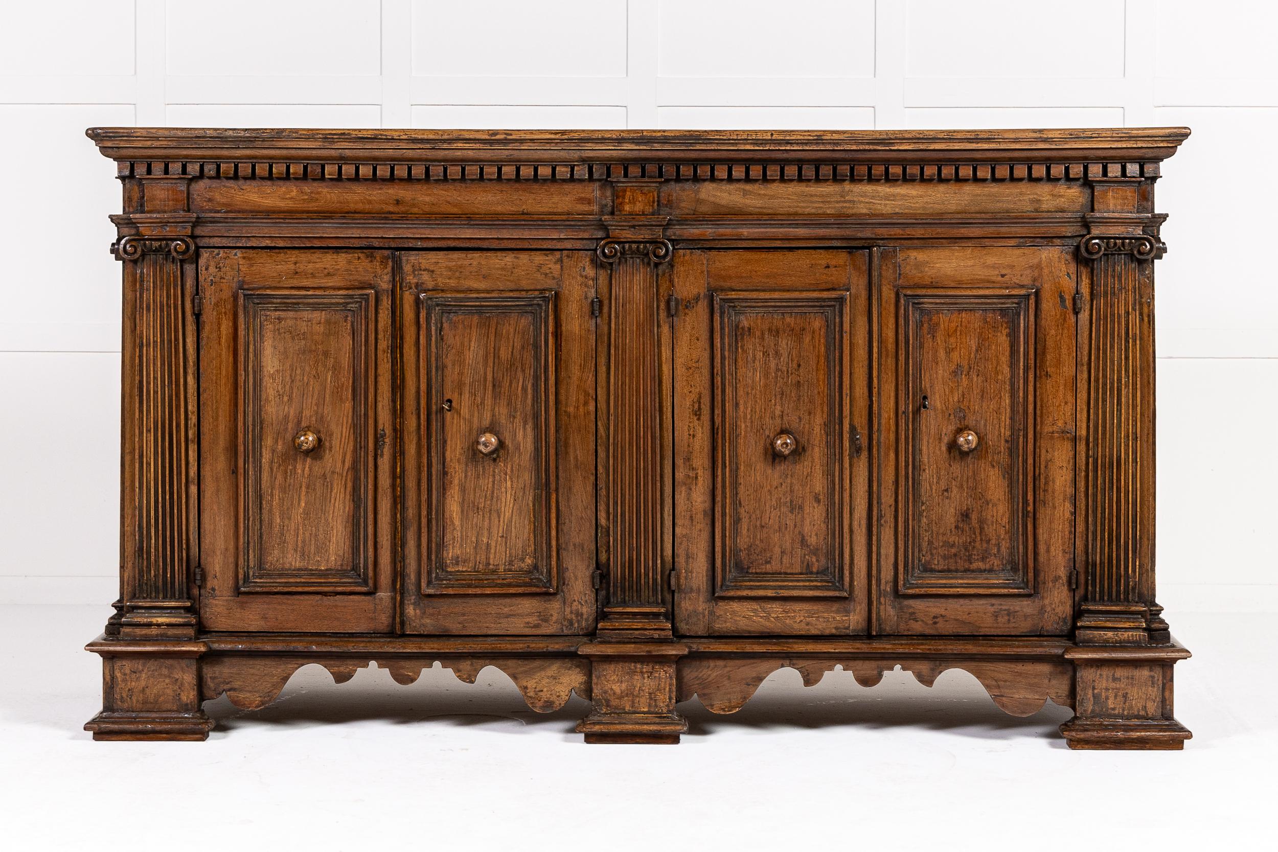 Inusual mueble auxiliar italiano del siglo XVIII, de cuatro puertas y madera de nogal, con detalles arquitectónicos.

Este extraordinario mueble tiene una encimera de tablones lisos con un friso dentilado que recorre el frente y los lados de la
