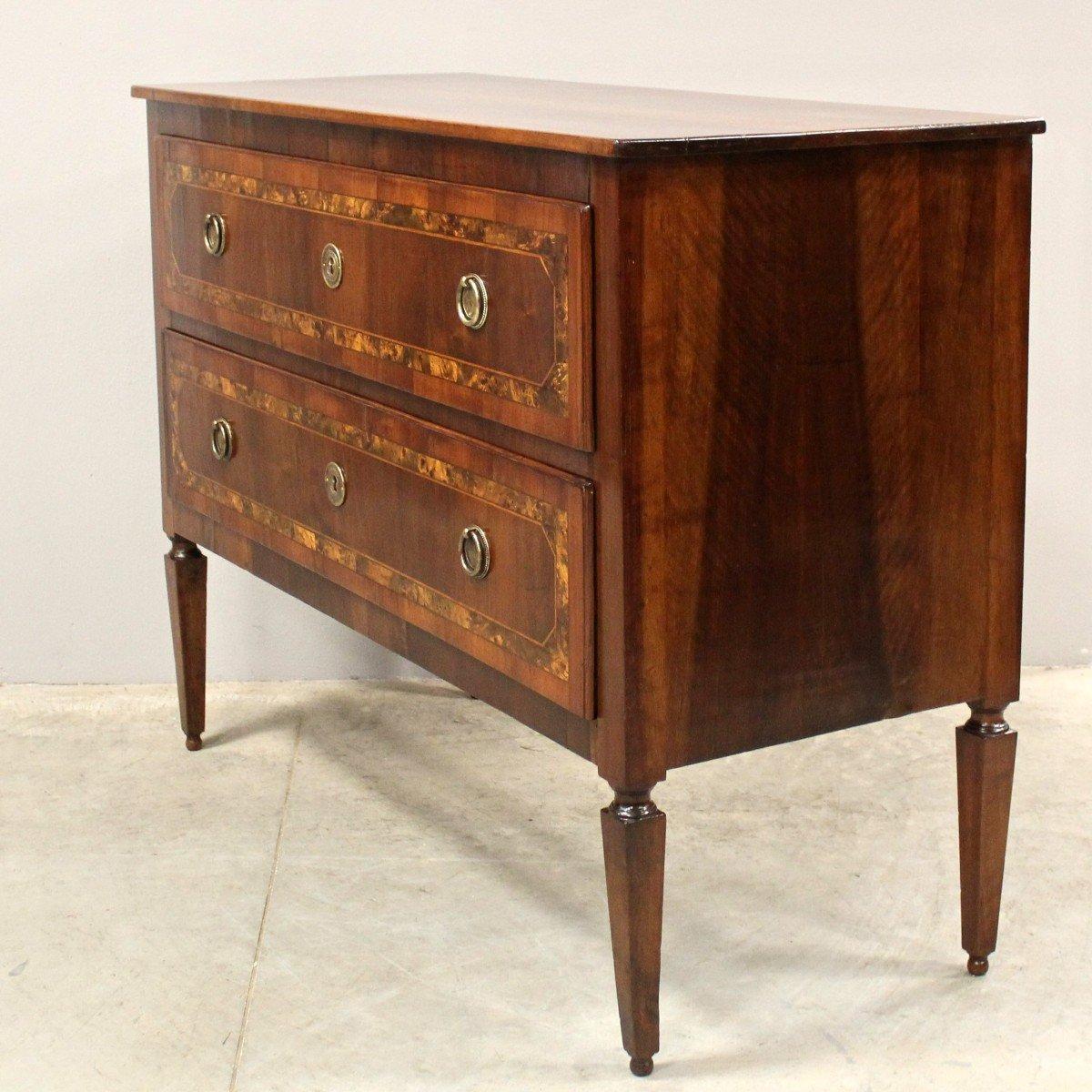 An Italian walnut commode from the 18th century with two drawers and tapered legs. Step into the world of Italian craftsmanship with this exquisite 18th-century walnut commode. The walnut construction emanates a rich, deep hue, perfectly contrasted